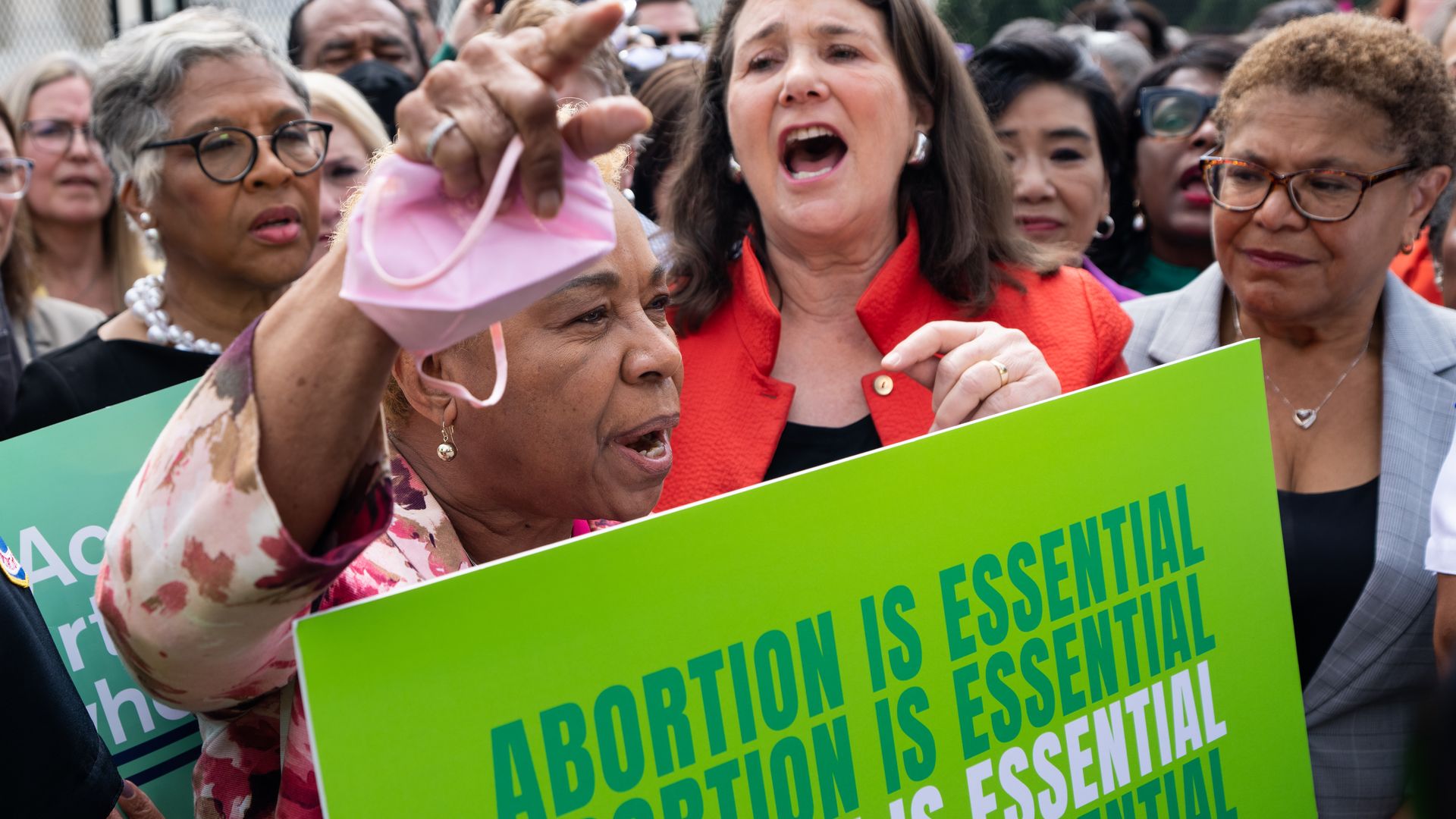 Photo of women lawmakers holding signs that say "Abortion is essential" at a protest