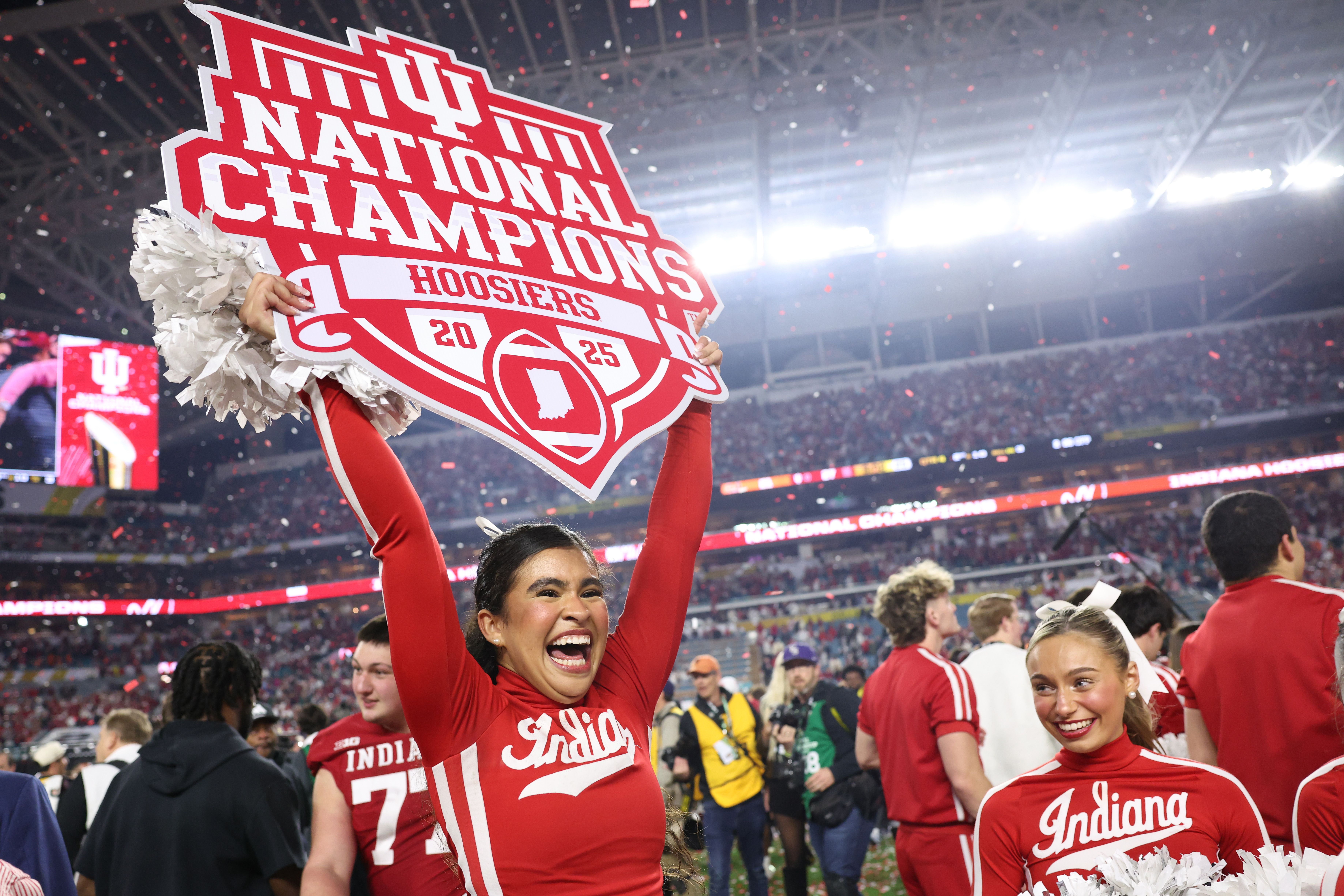 Cheerleaders celebrating Indiana Hoosiers 2025 National Champions with red and white outfits and pom-poms inside a crowded stadium with confetti falling.