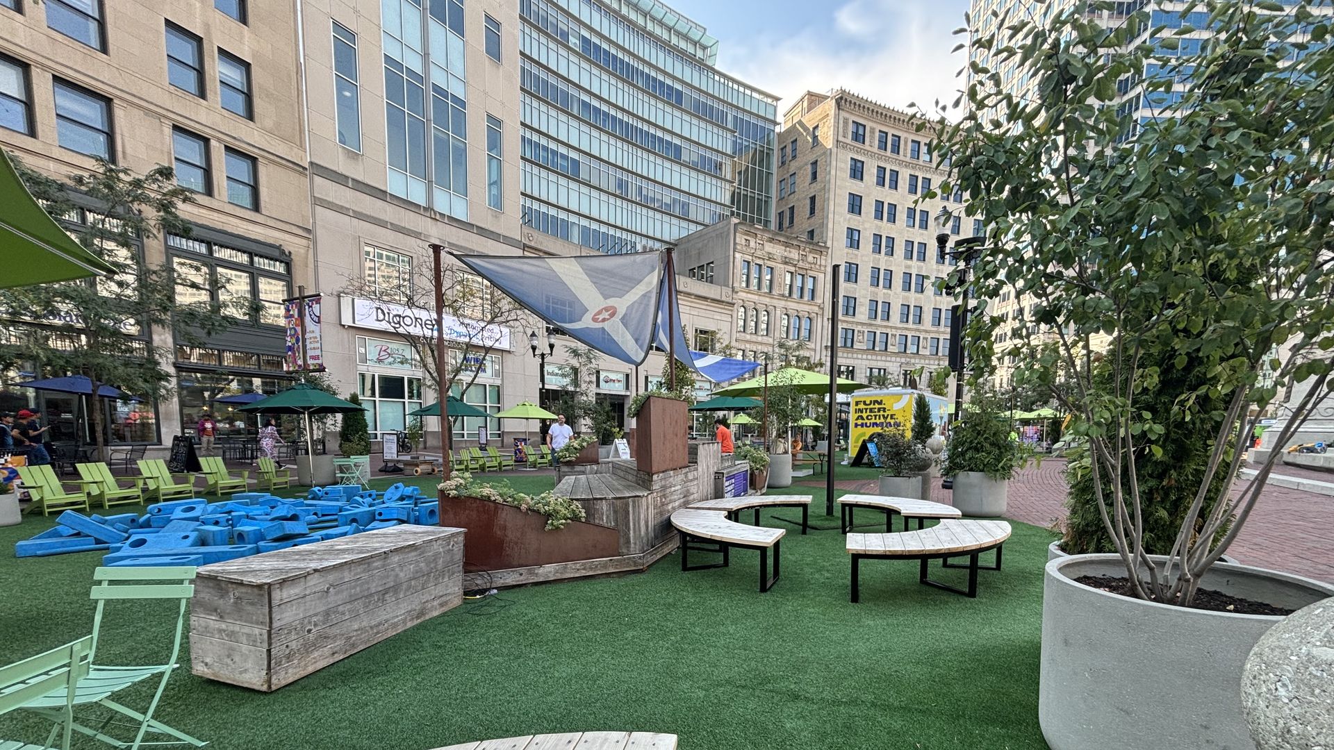 Turf surrounded by buildings and tables and trees. 
