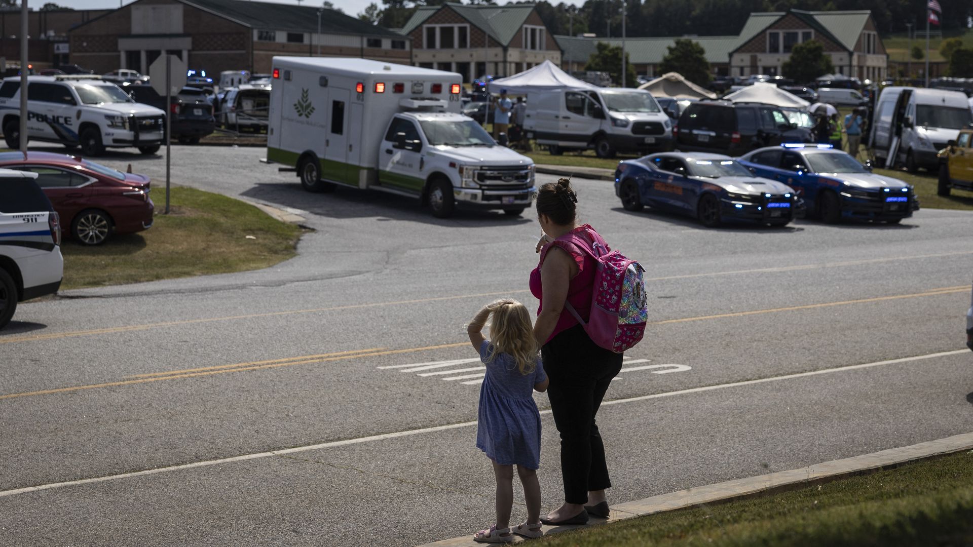 A young girl and her mother watch as law enforcement and first responders surround Apalachee High School in Winder, Georgia, on September 4, 2024, after a shooting was reported.