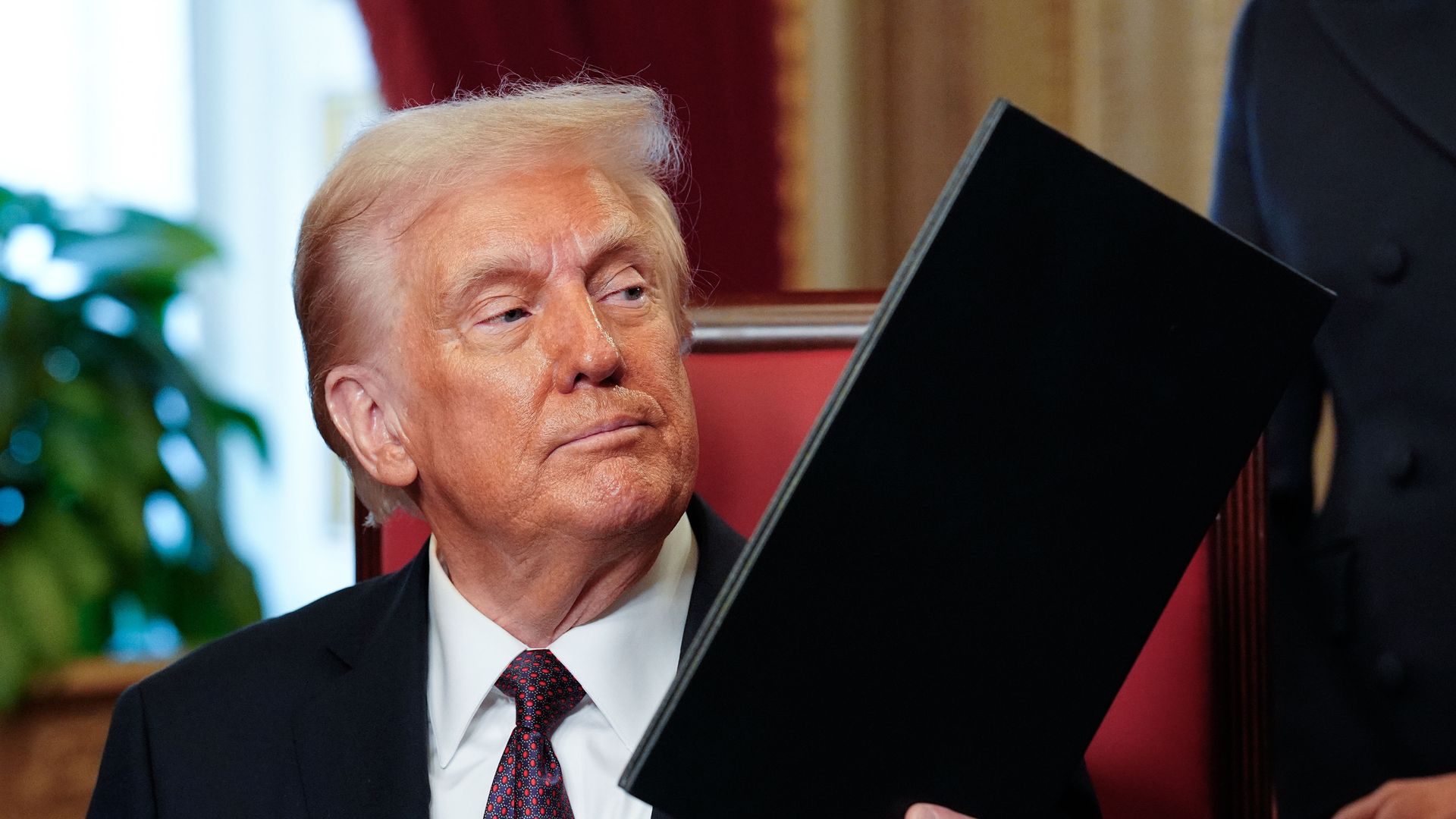 Trump holds a folder in one hand 