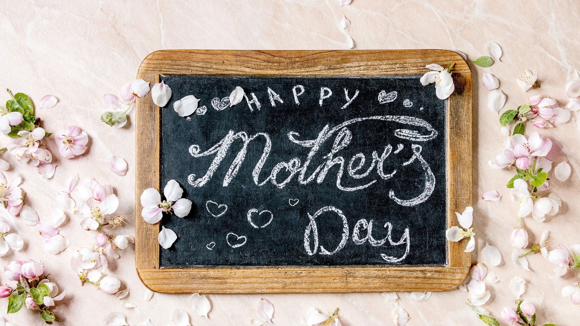 Mother's day greeting card. Vintage chalkboard with handwriting lettering Happy mother's day with spring apple flowers and petals over pink marble background. Flat lay, space.