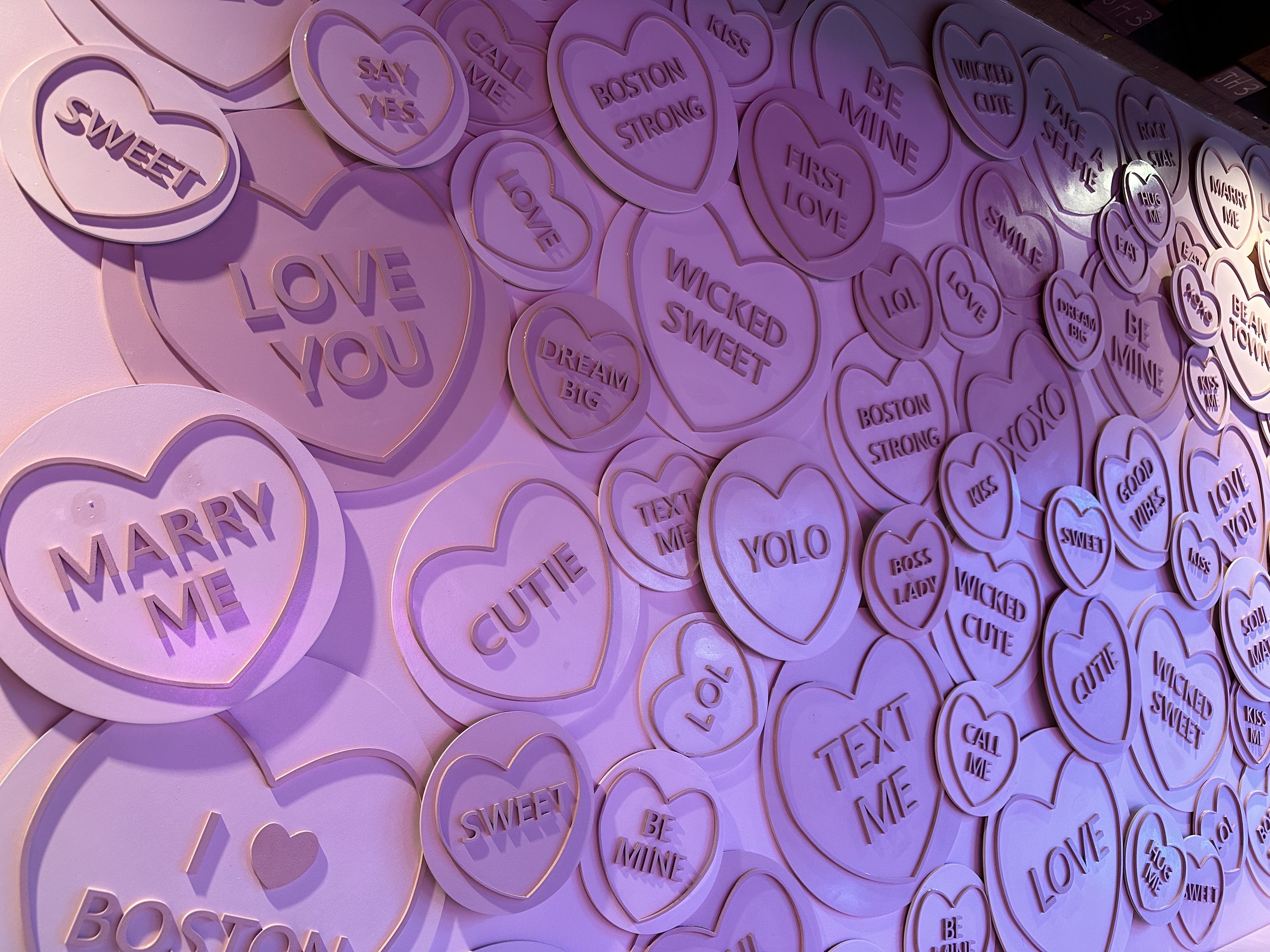 A wall with several messages in pink hearts in the Sugar Factory's "pink room." The hearts say "sweet," "marry me," "YOLO," "wicked sweet" and more.
