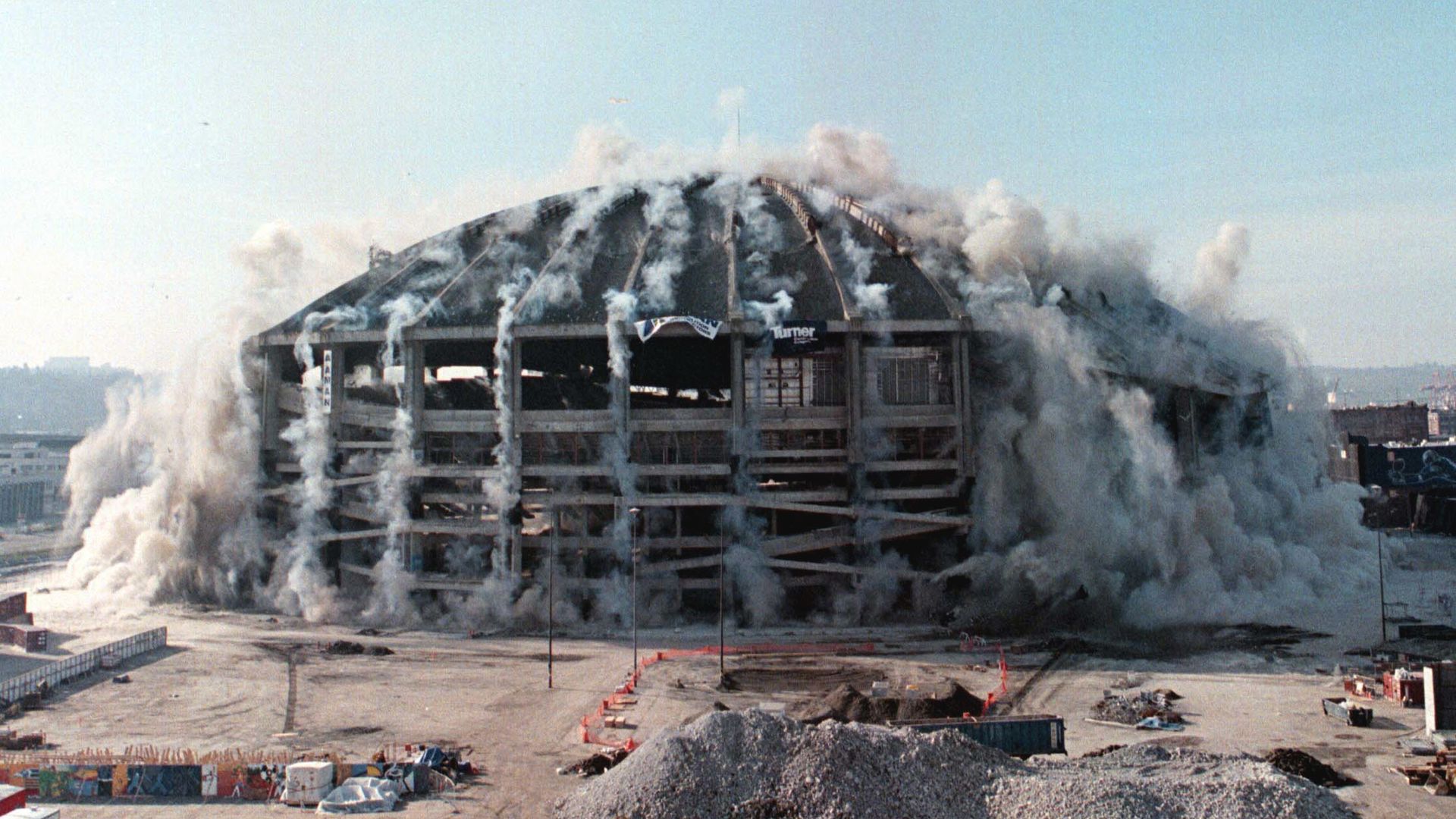The Kingdome is shown as it just starts to implode, with the structure sinking and dust and debris starting to spread.