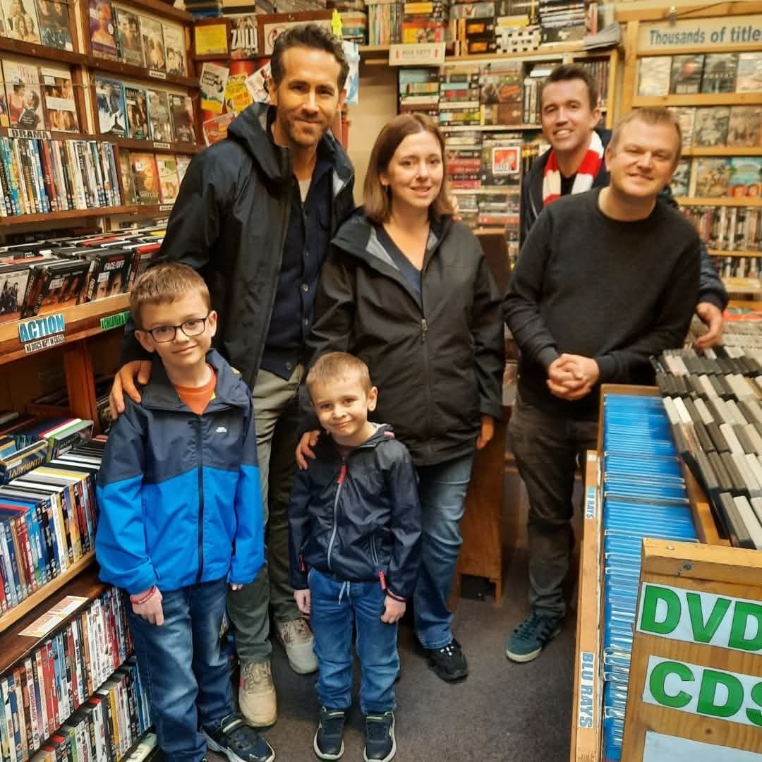 Mad4Movies owner Rob Clarke, right, with his wife and sons, posing inside their DVD shop with actor Ryan Reynolds and Rob McElhenney.