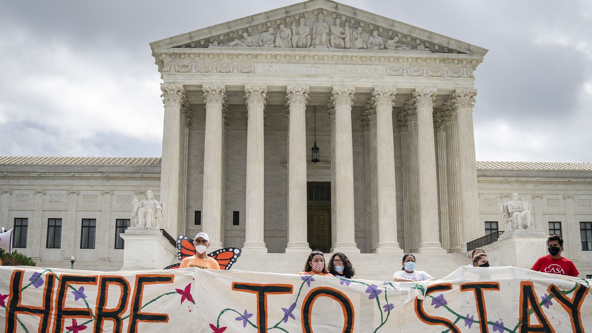 Immigration activists hold a banner that says "here to stay" in front of the Supreme Court.