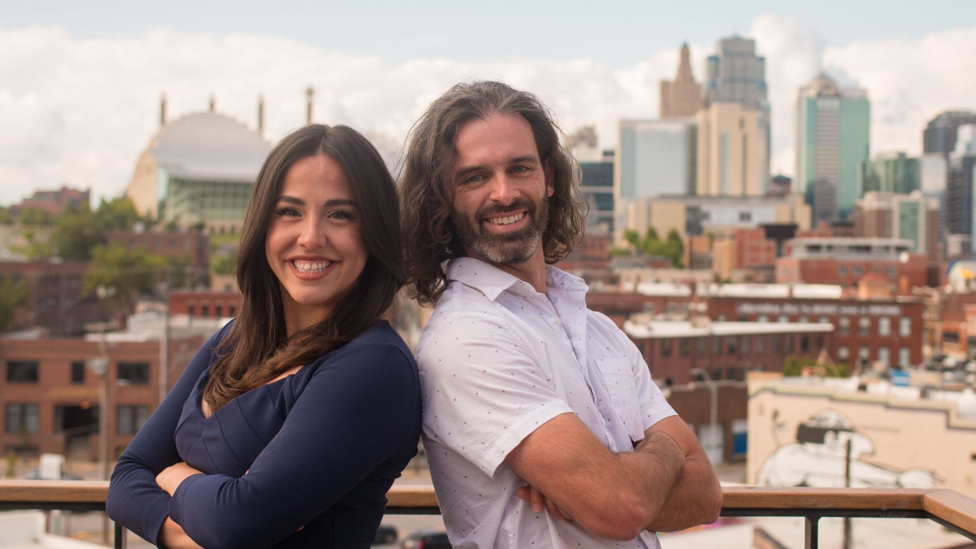 Axios reporters Abbey and Travis pose back-to-back with the Kansas City skyline in the background.