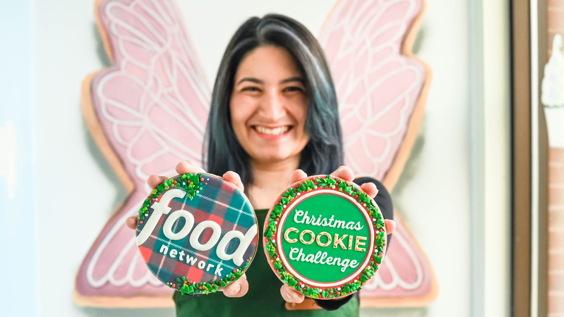 person holding up two round cookies decorated with icing that reads "food network" on one and "christmas cookie challenge" on the other