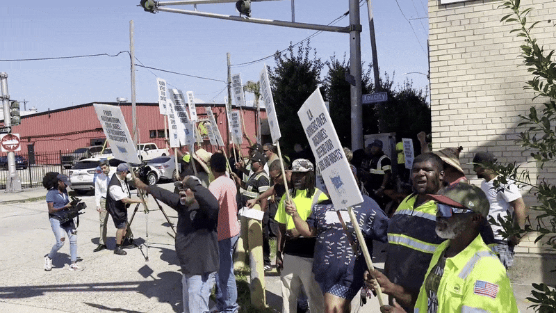 A moving image shows workers raising signs in a picket line.