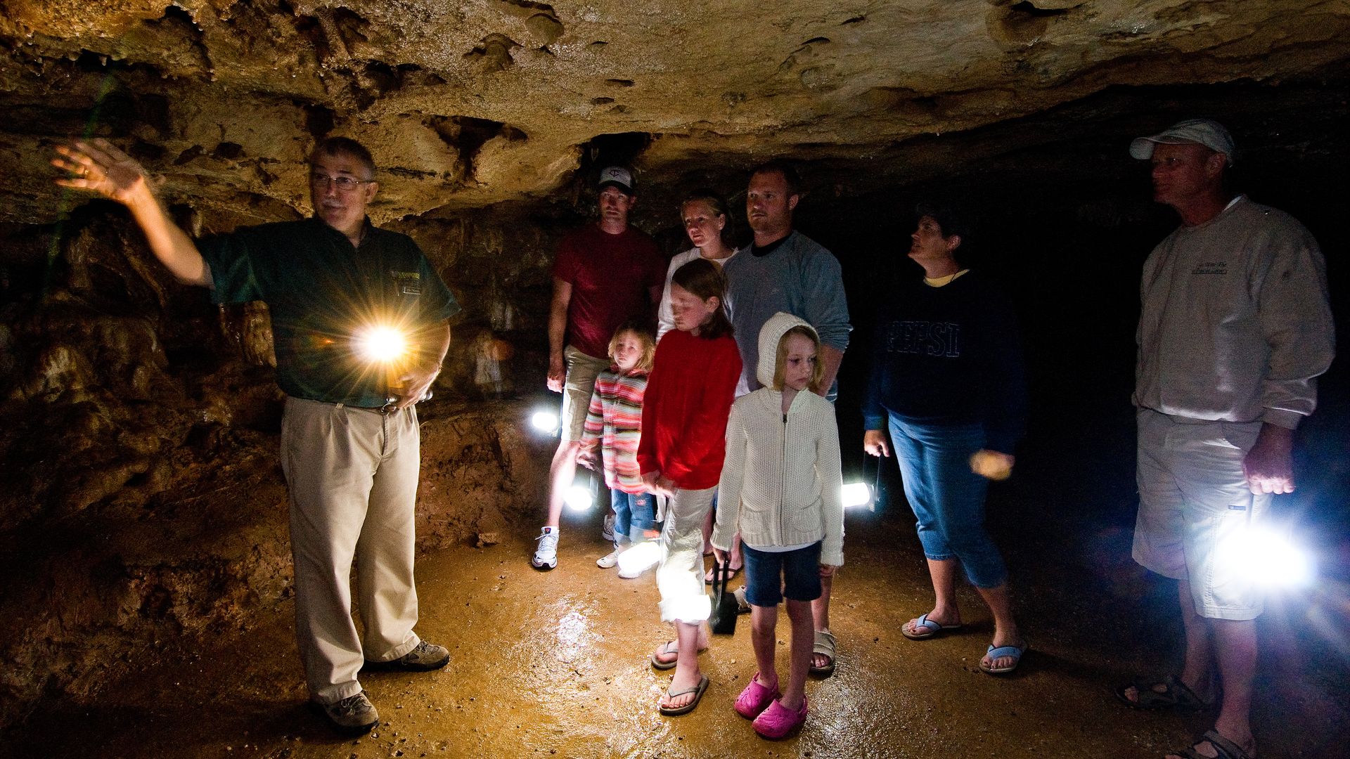 A group of tourists with flashlights look over the inside of a cave. 