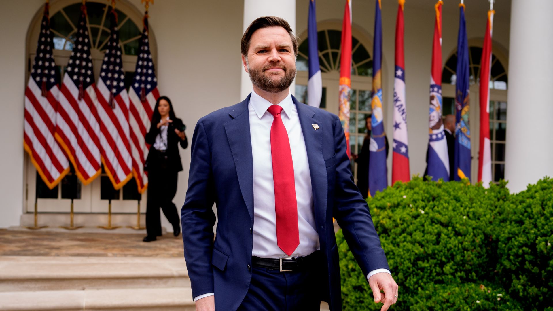 JD Vance arrives for an event in the White House Rose Garden with several state and American flags in the background.