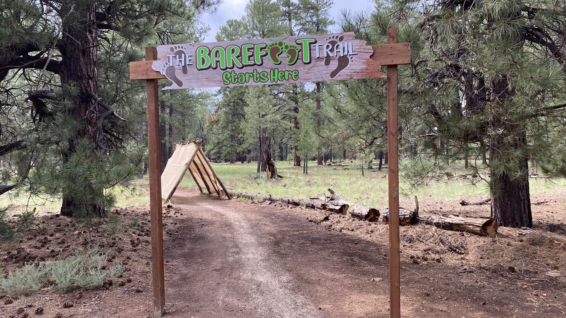 A trail with a line of sand running down the middle with a sign above it that says Barefoot Trail.