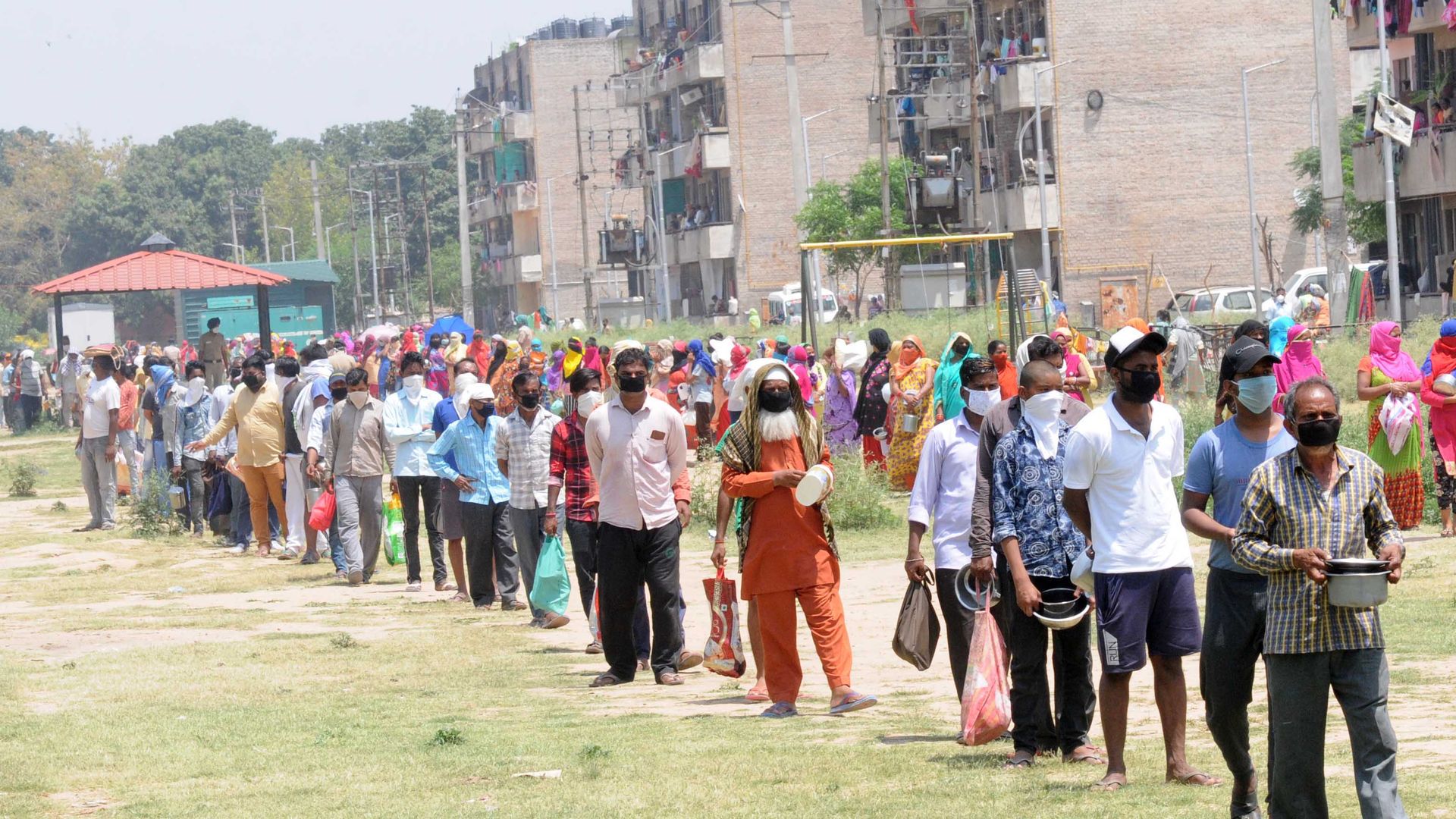 In this image, a long line of masked people stand in line outside