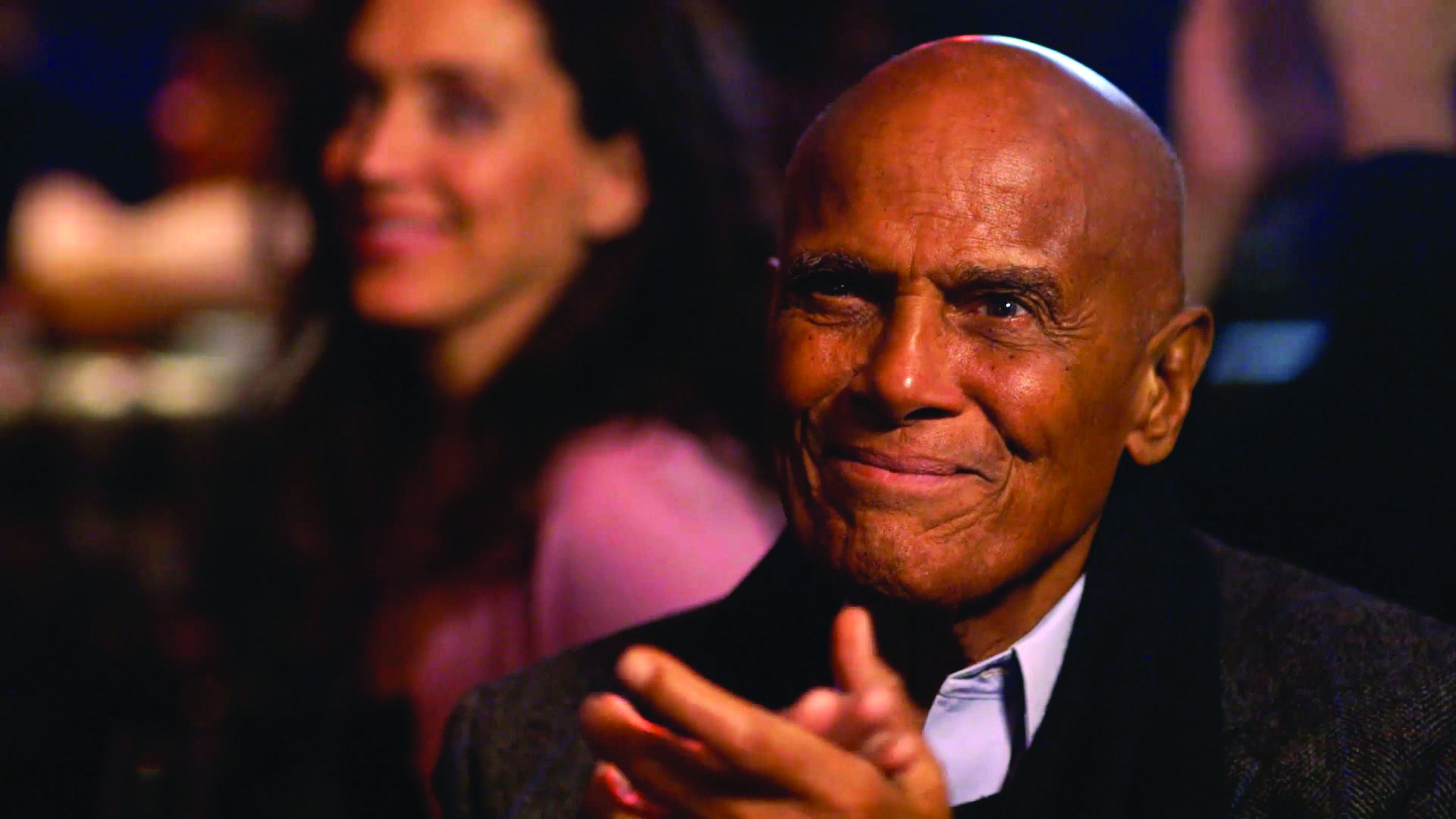 Harry Belafonte applauds while in a crowd.