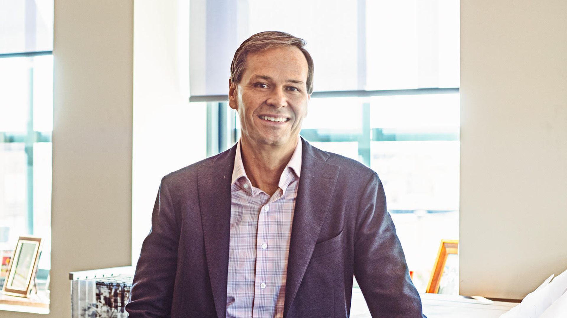 A man in a suit jacket standing against a desk.