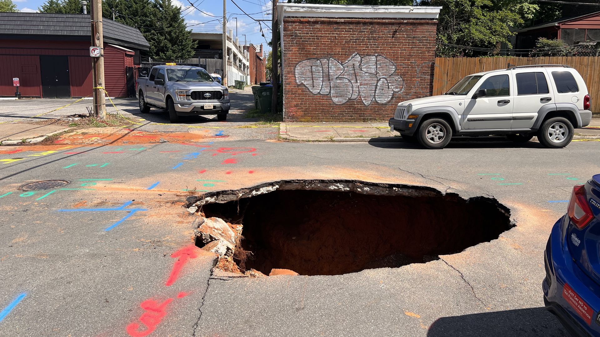 A massive sinkhole on a city street surrounded by cars.