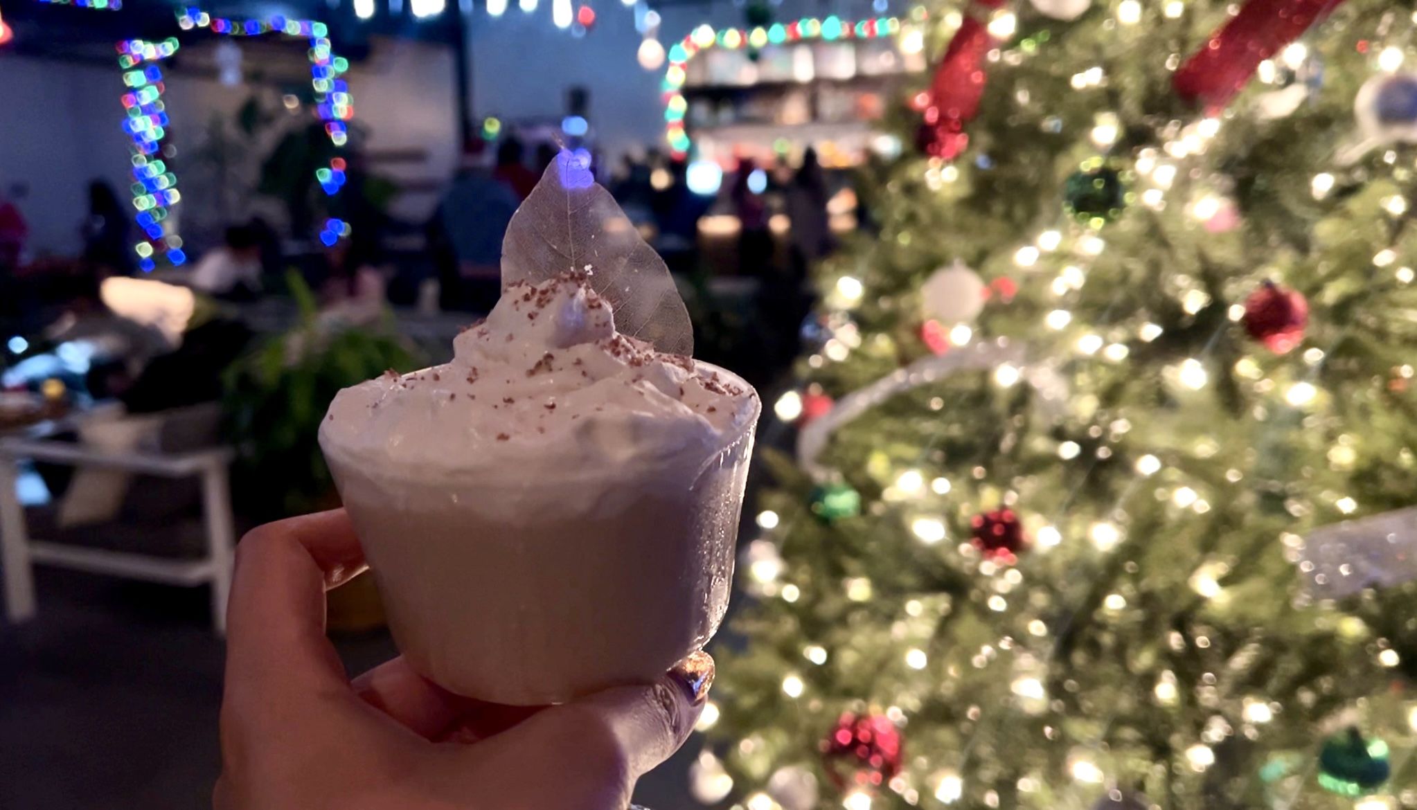 A person holds a small cocktail glass with a drink topped with whip cream.