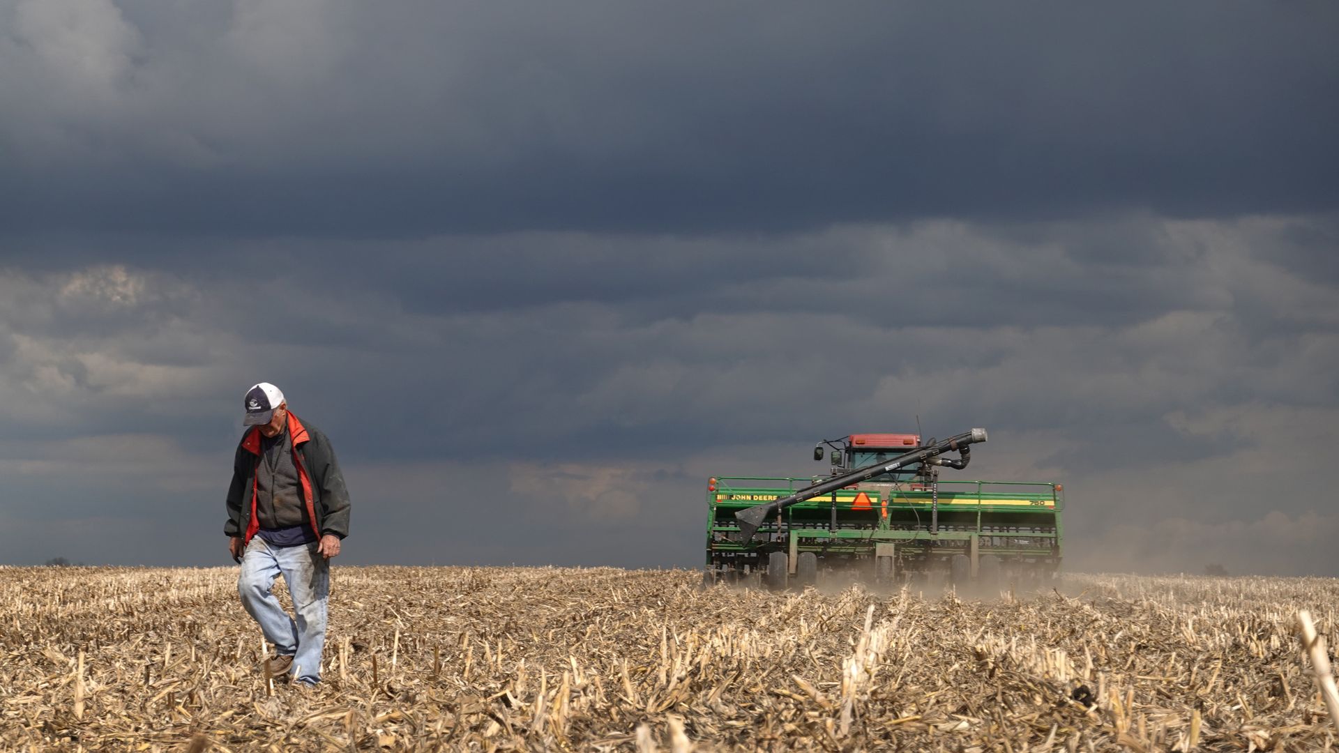 Photo of a farmer walking on his open land with a big tractor behind him. 