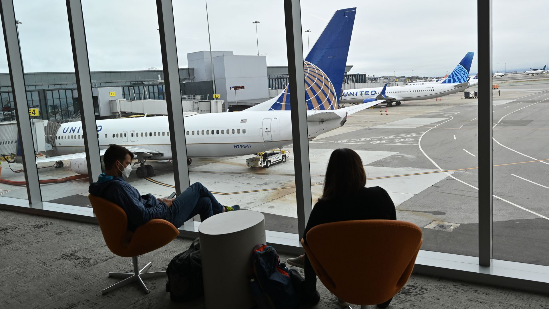 Two people sit inside the airport with plans in the background.