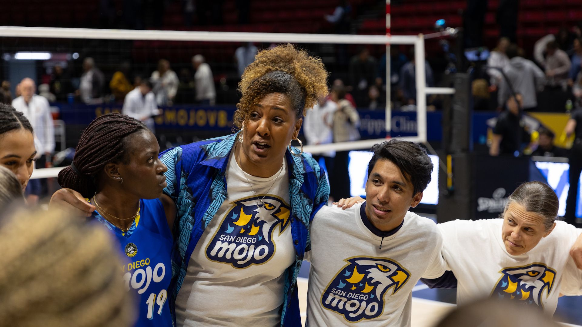 A women's volleyball coach talks to players in a huddle.