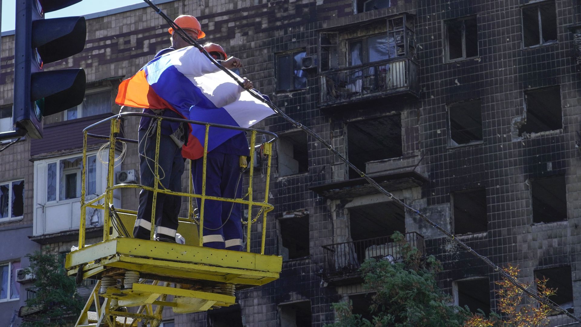  Workers fix a Russian national flag on wires with a damaged building in the background in Mariupol on September 25.