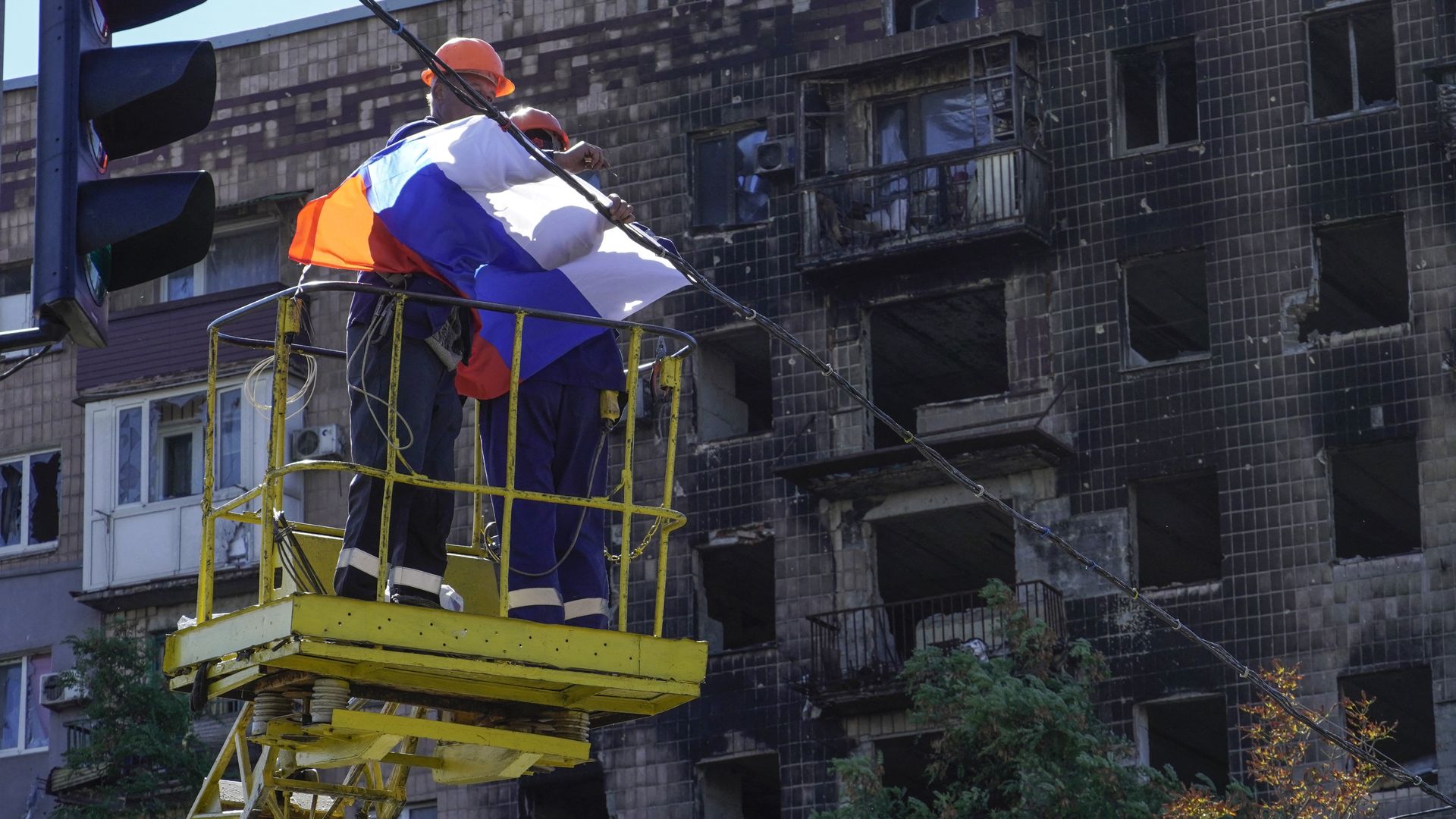 Workers fix a Russian national flag on wires with a damaged building in the background in Mariupol on September 25.