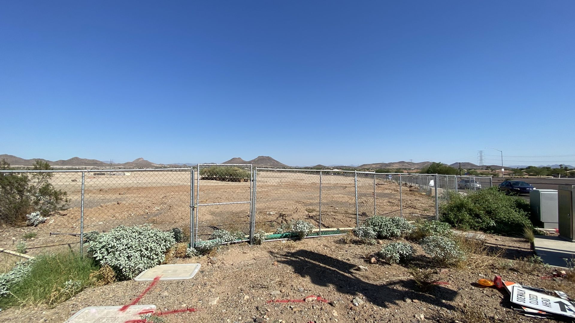 A large of plot of dirt surrounded by a chain link fence, with mountains in the background.