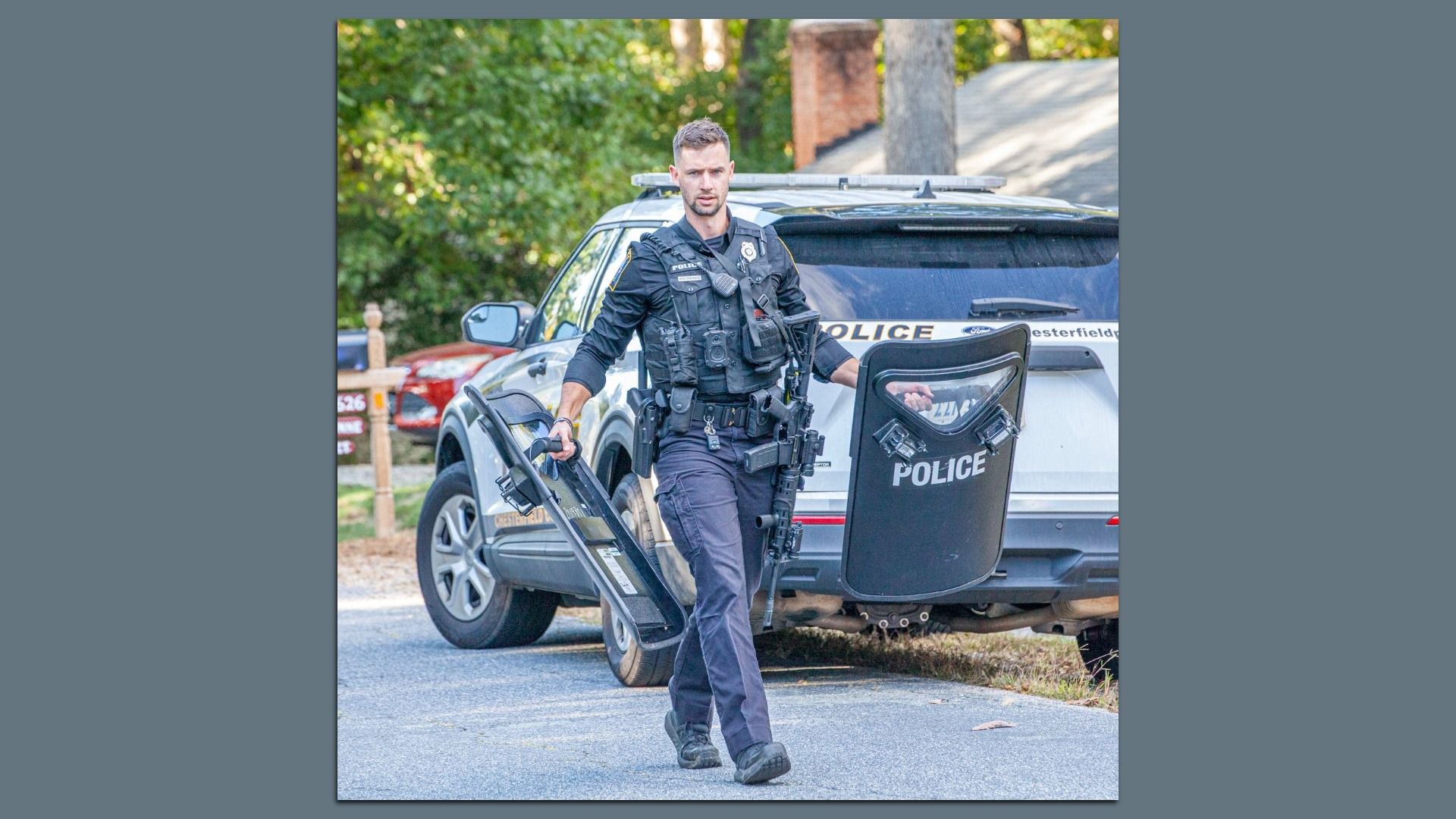 a police officer walks down a street holding a shield and machine gun  