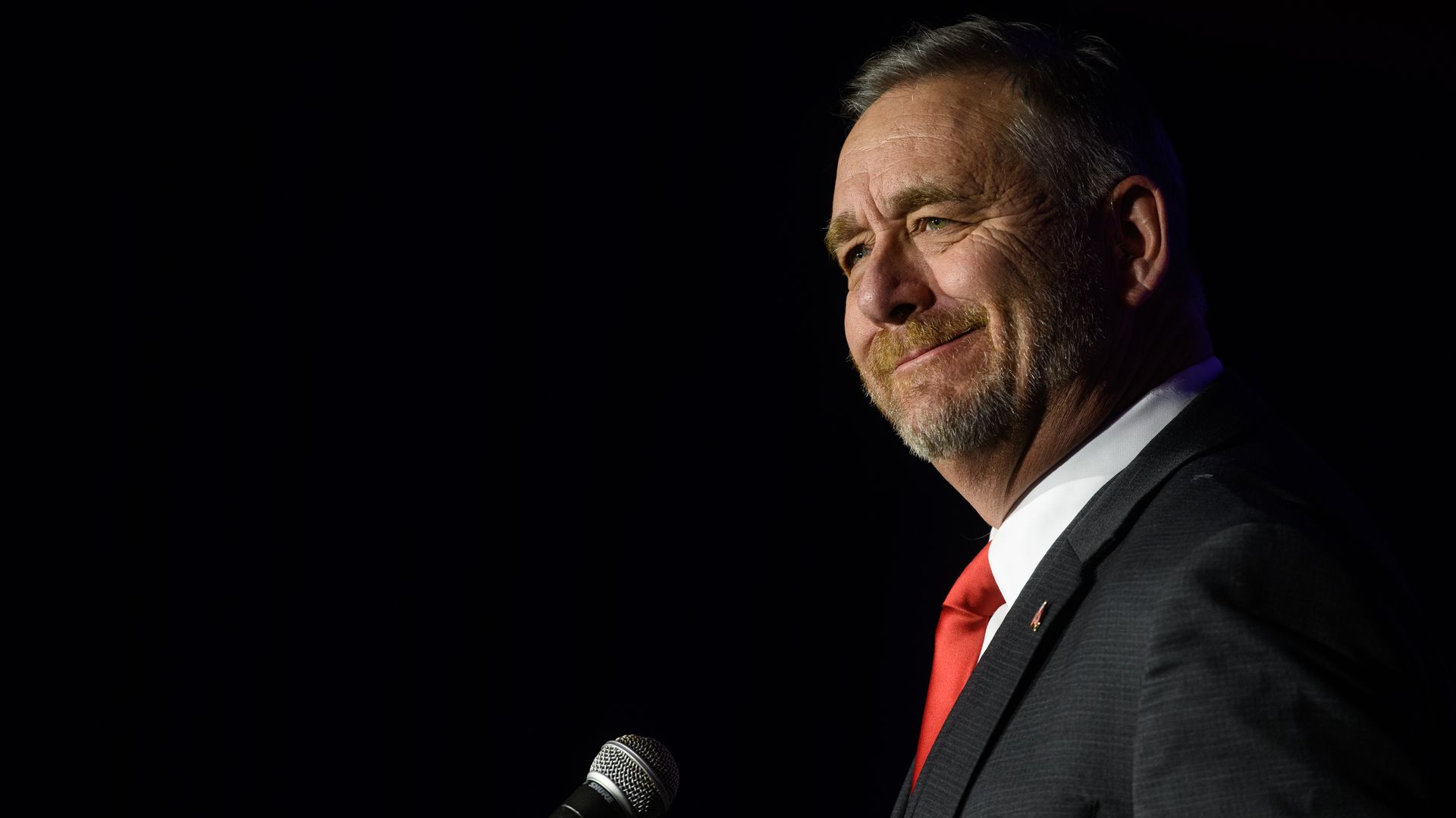 Dave Yost stands in front of a microphone wearing a suit and tie. 
