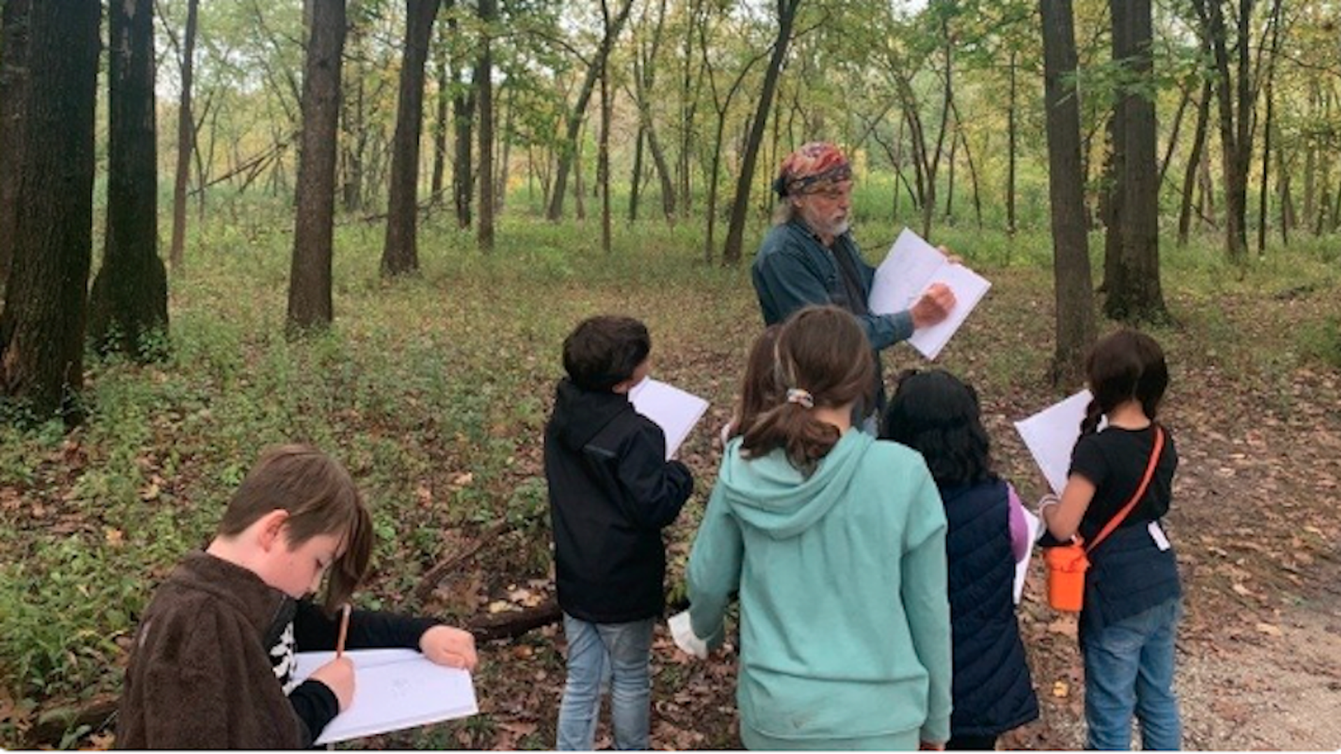 Photo of a teacher leading class in the woods. 