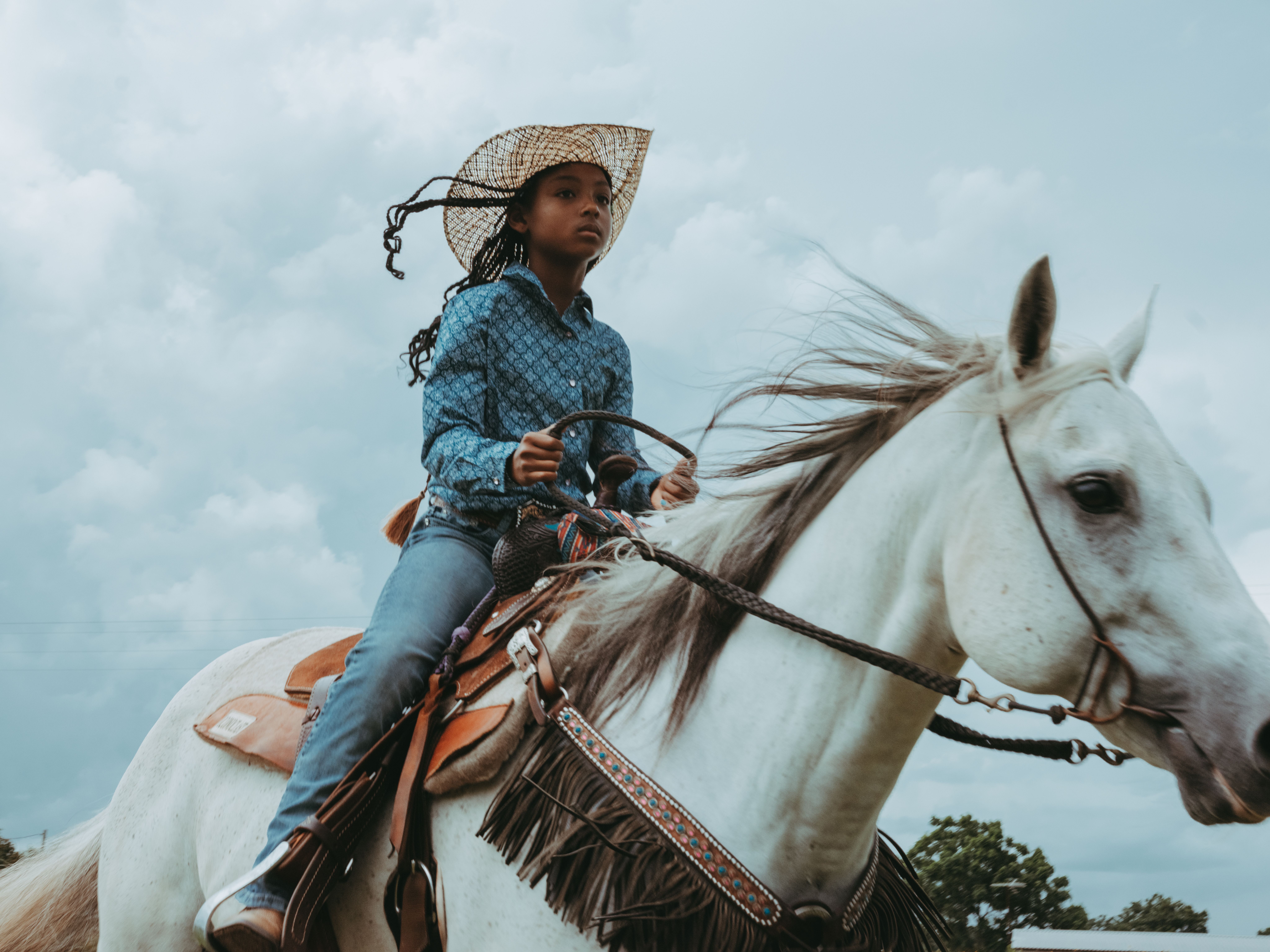 Photo of a young Black girl riding a white galloping horse.