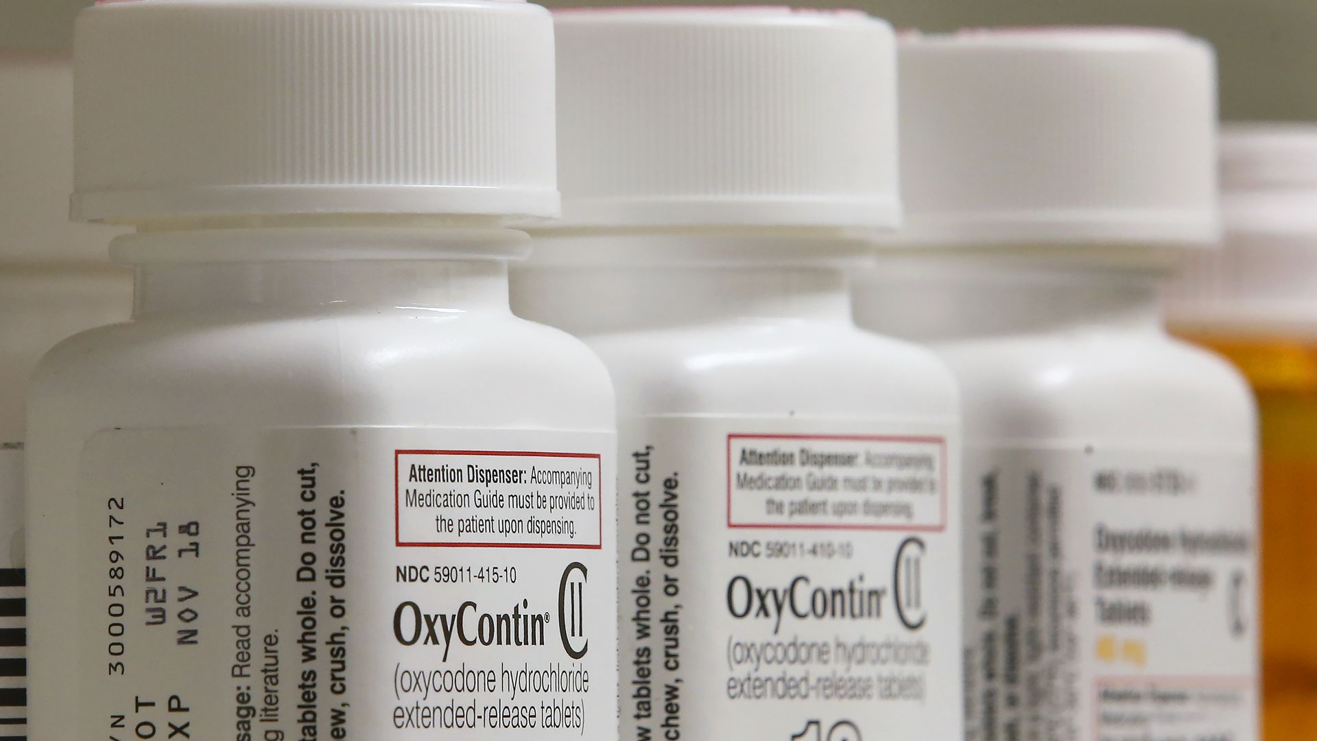 Close-up of white prescription bottles of OxyContin with dosages 15 mg and 10 mg visible, showing warnings and medication guide instructions on labels.