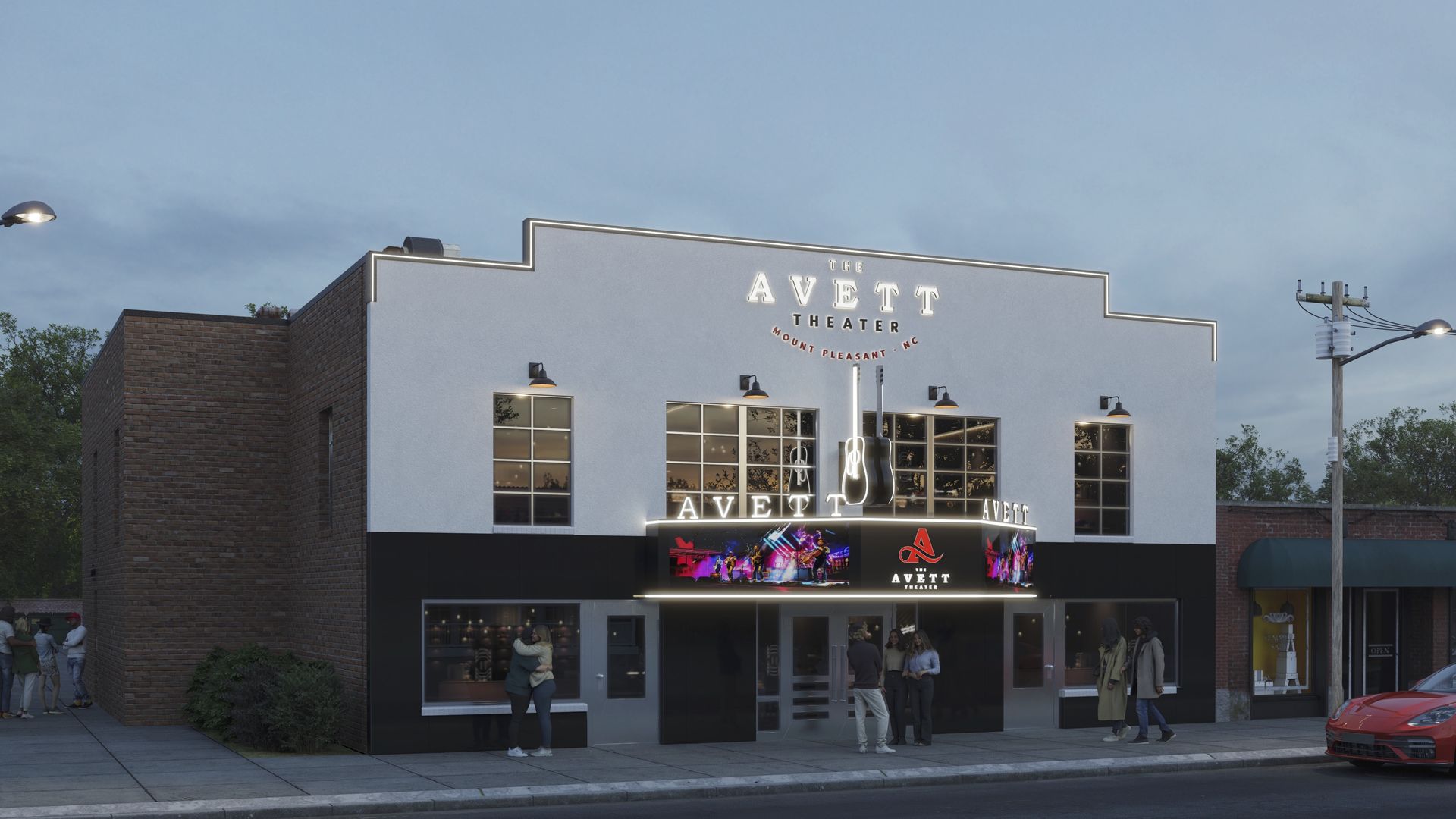 The Avett Theater in Mount Pleasant, NC, is a white and black building with neon-lit sign and two large guitars above the entrance. People stand near the entrance and a red car is parked nearby.