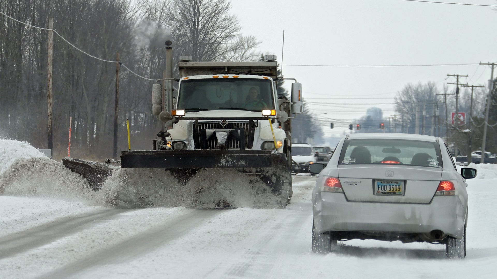 A snow plow clears off a two-lane road. 