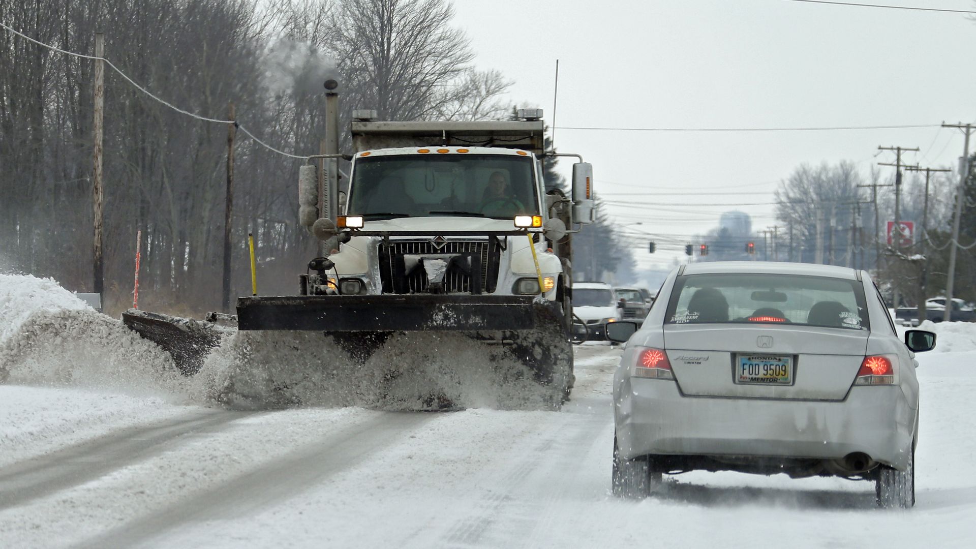 A snow plow clears off a two-lane road.