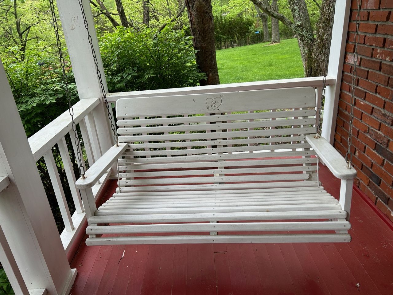 A wood porch swing painted white with a heart and a pair of initials etched onto the back