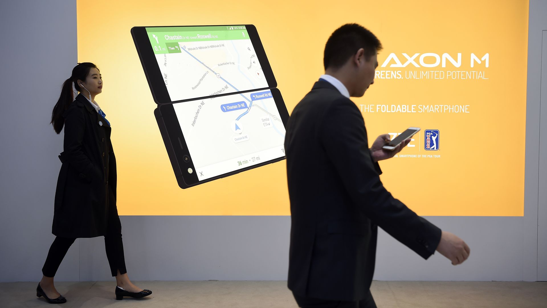 Two people walk past a billboard announcing the new ZTE's dual screens foldable smartphone AXON M