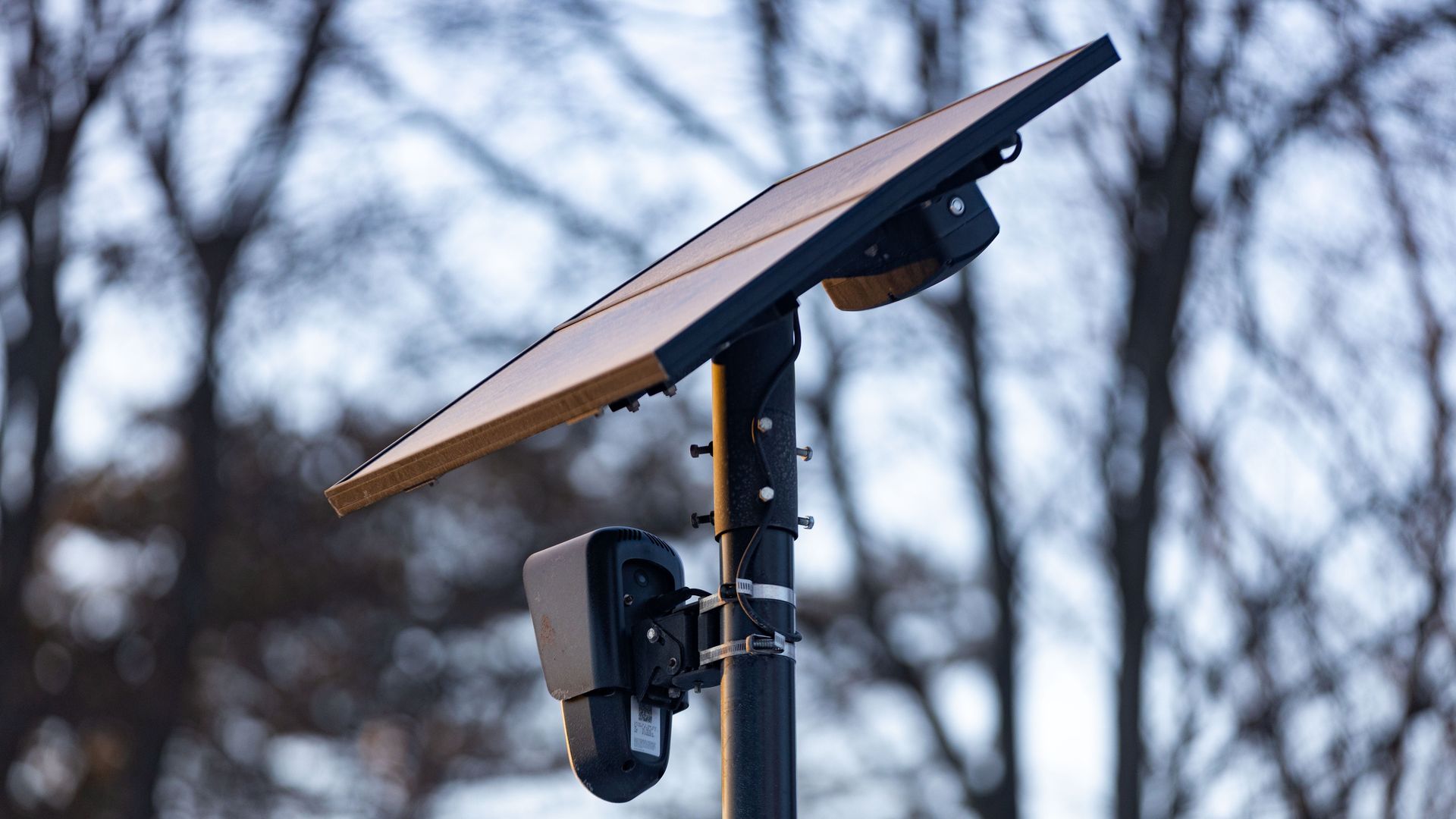 A Flock Safety license plate reader system is seen in the foreground, with trees in the background.