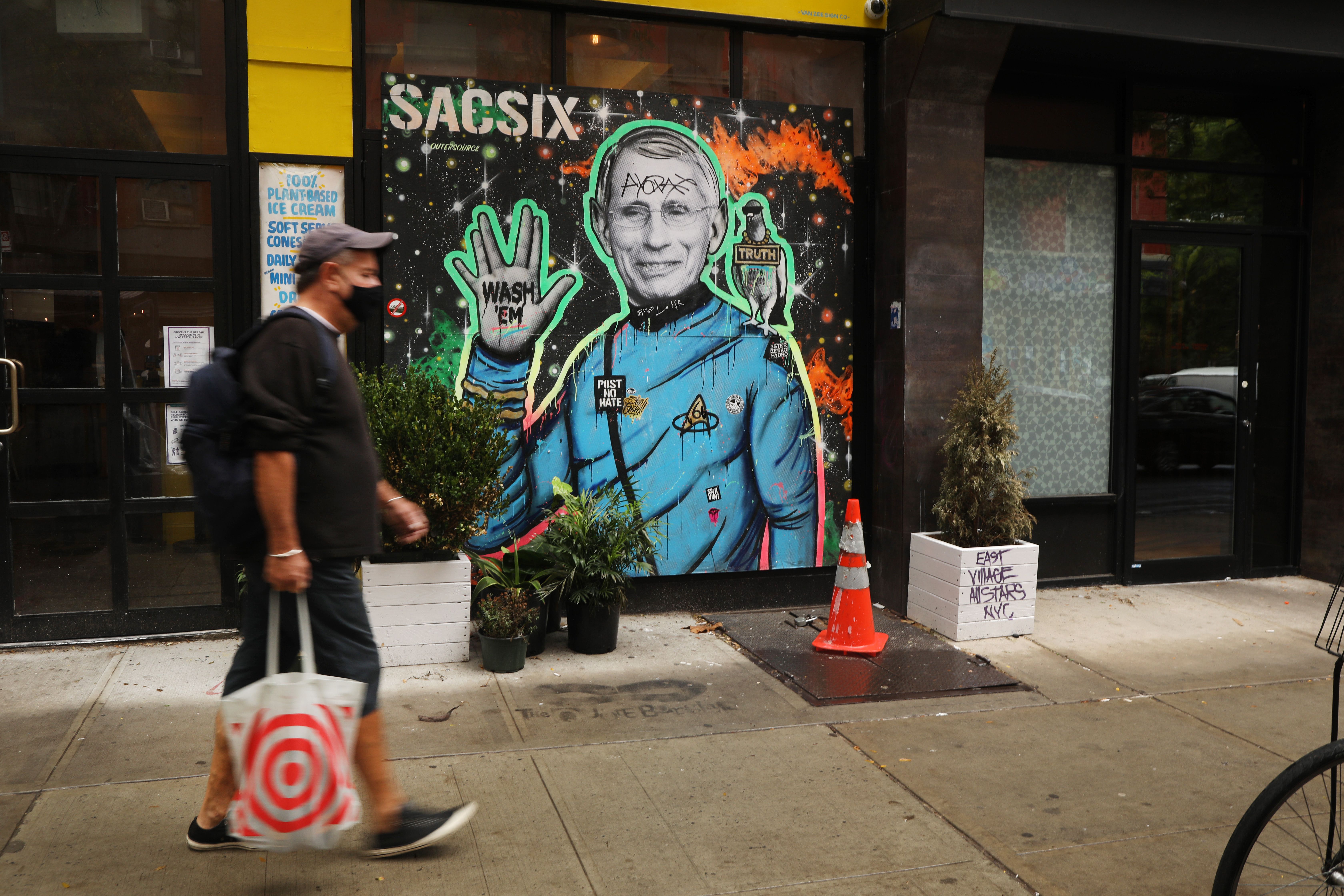 People walk past a mural of Dr. Anthony Fauci by the artist SacSix on October 20, 2020 in the East Village of New York City. 