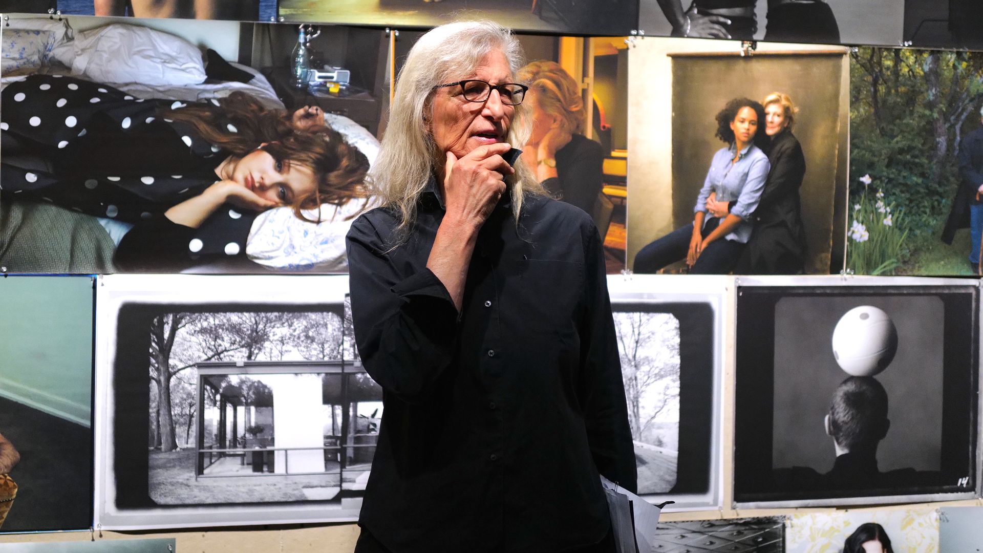 Photographer Annie Leibovitz stands in front of several of her photographs on display at a museum.