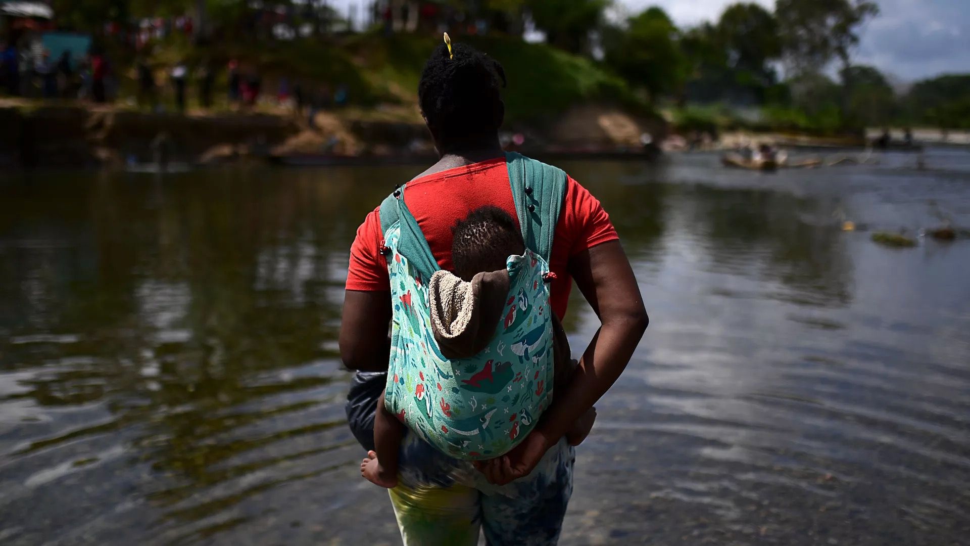 A migrant is seen carrying a baby across the Chucunaque River after walking for five days in the Darien Gap.