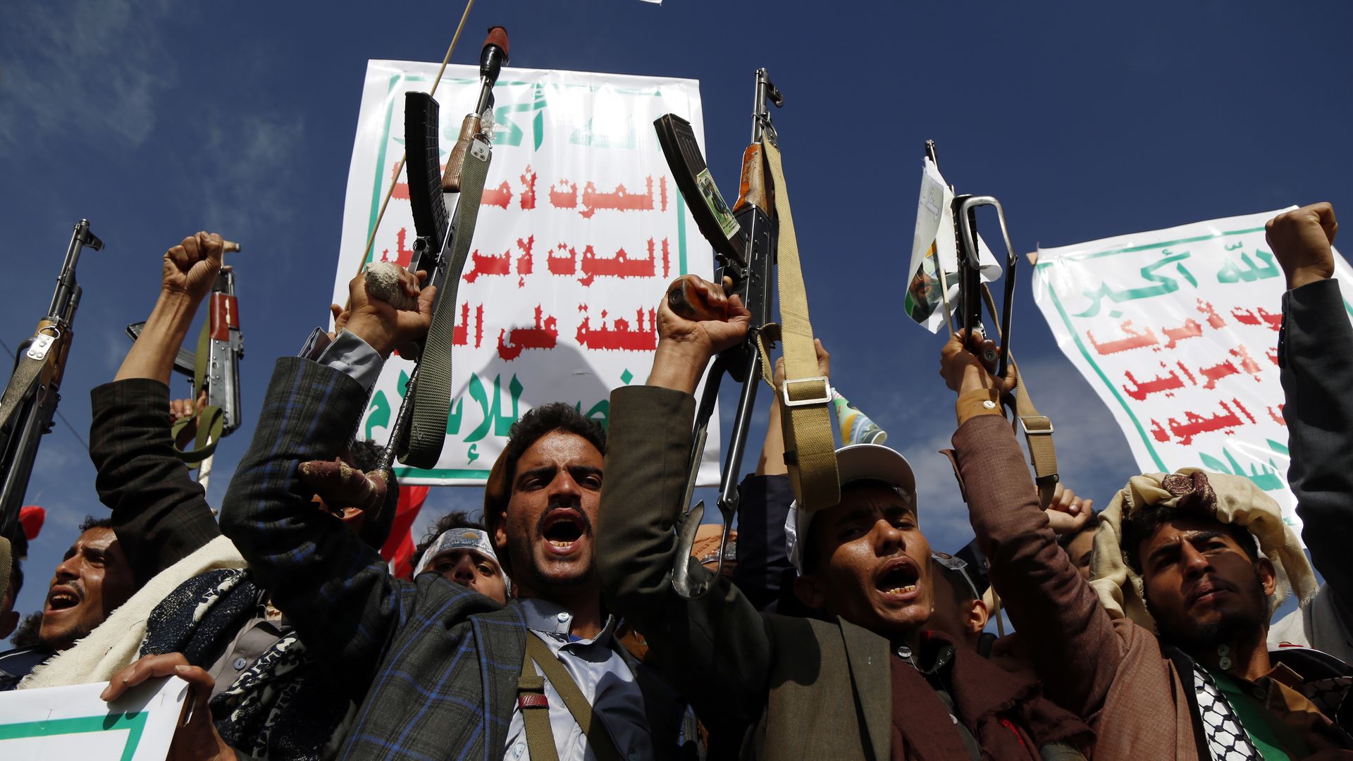 a crowd of protestors holding guns, flags and signs