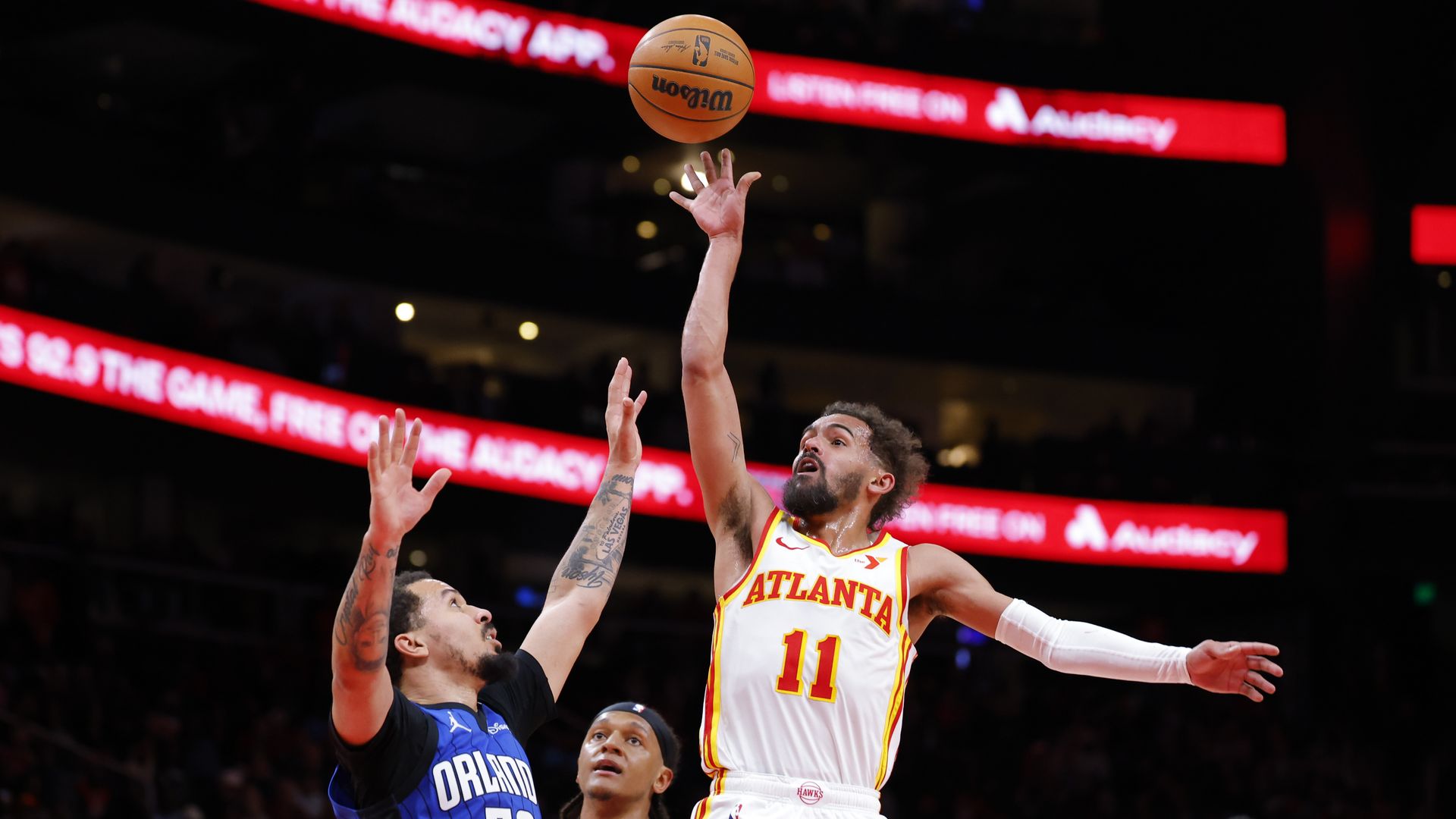 Trae Young in a white basketball uniform shoots over an Orlando player