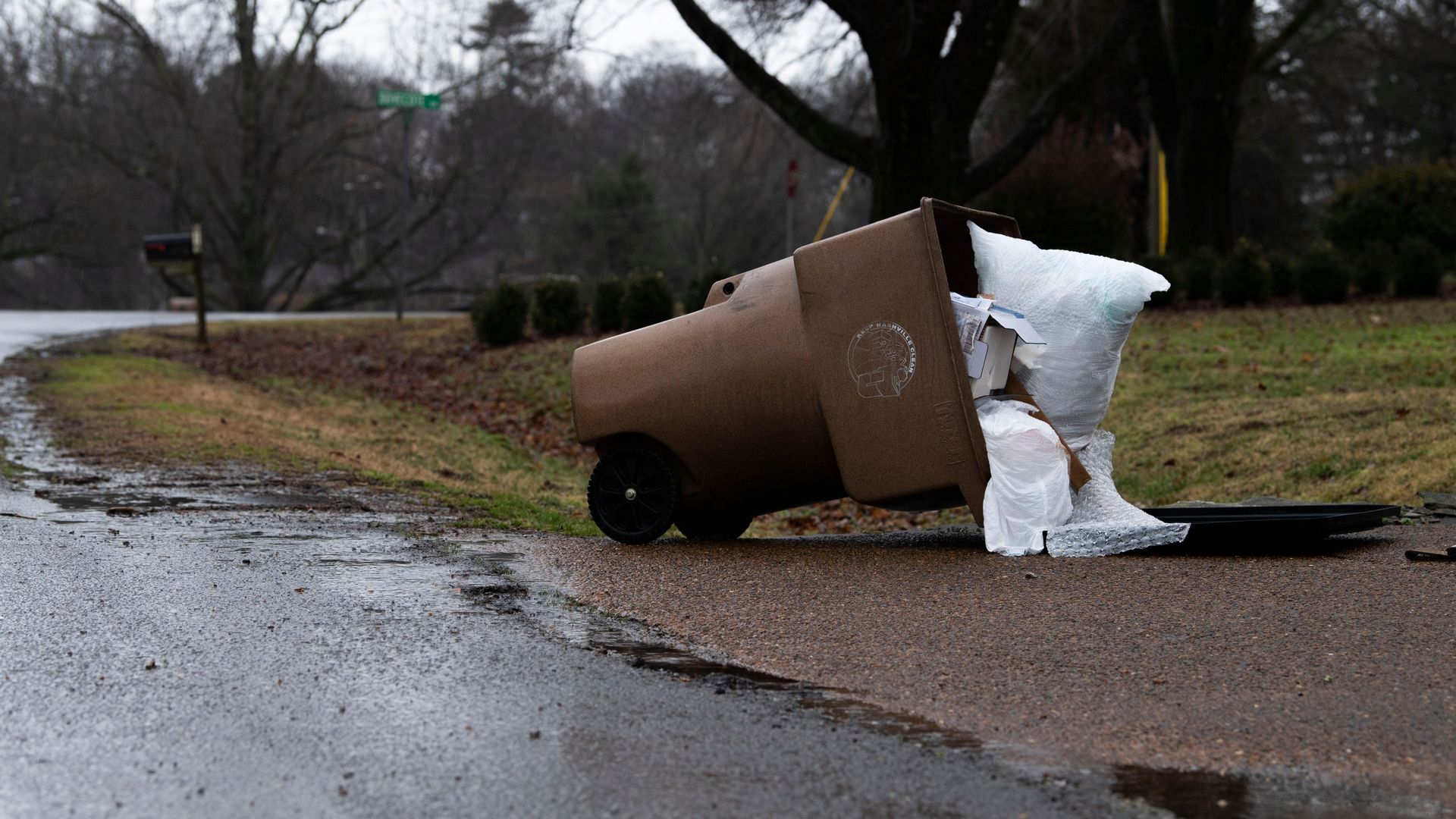 An overflowing trash can that tipped over, with bags spilling out.