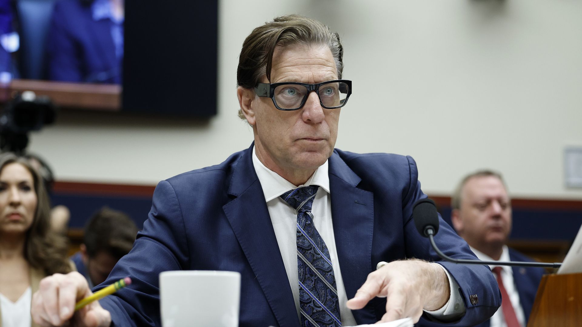 Richardson wearing a blue suit jacket, white shirt, blue tie and glasses