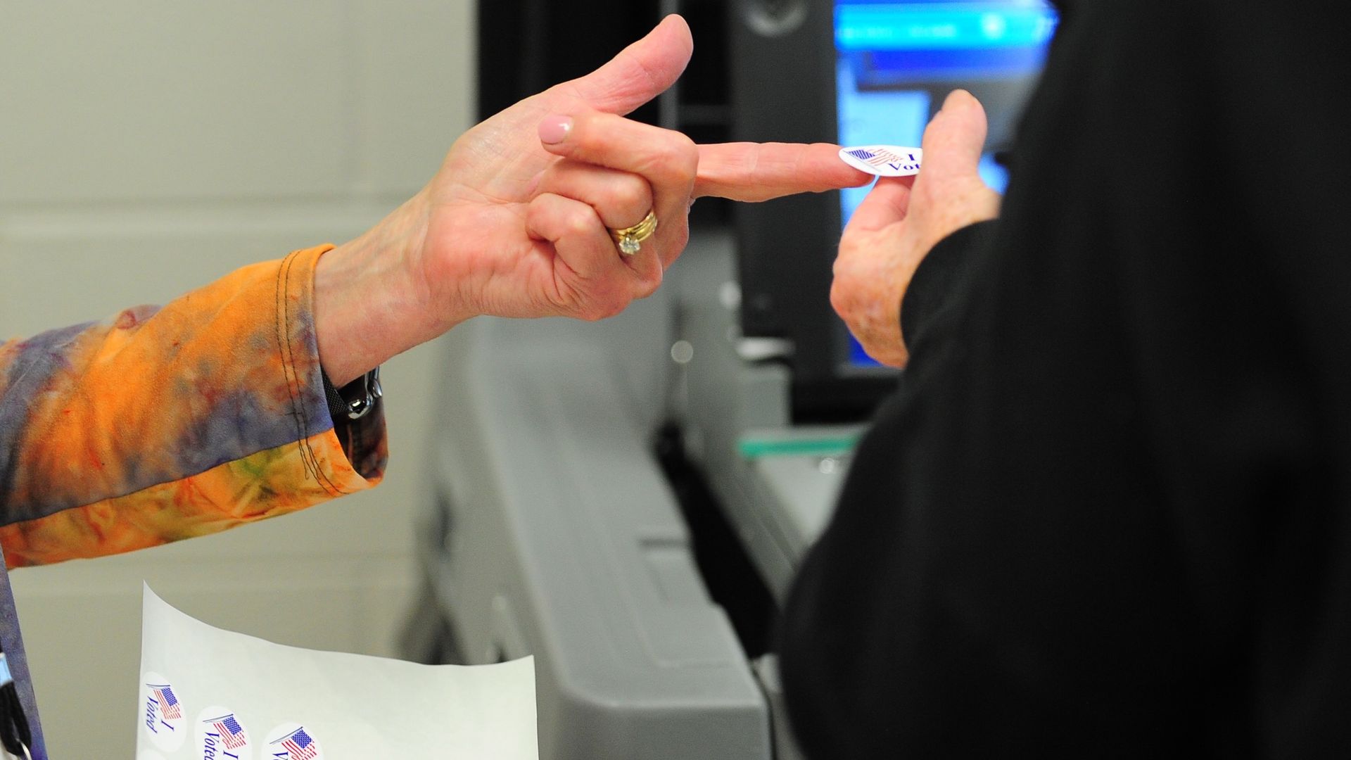 An election worker hands an "I voted" sticker to a voter. 