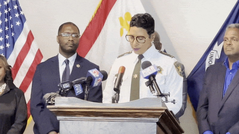 Michelle Woodfork, wearing an Orleans Parish Sheriff's Office uniform, speaks at a podium.