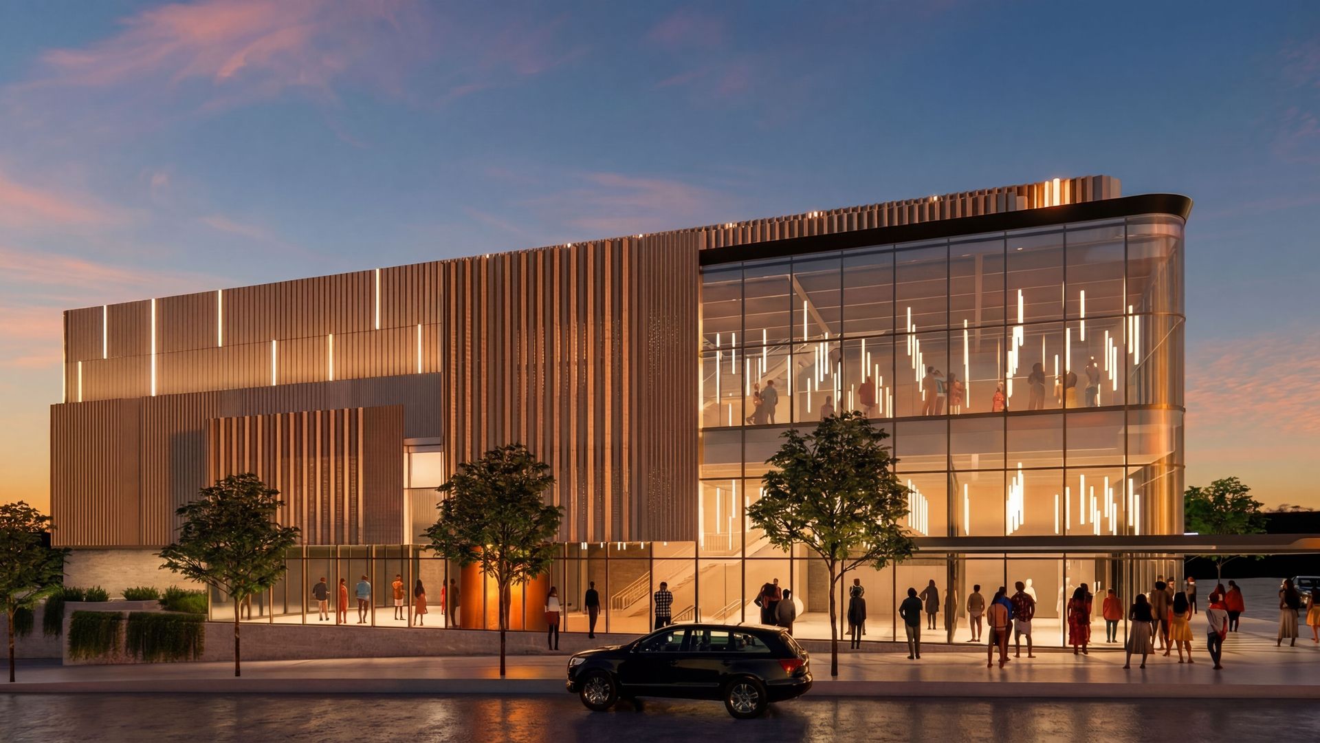 Modern two-story glass building with vertical wood panels and illuminated interiors visible through large windows; sunset sky, trees along the sidewalk, people outside, and a car by the curb.