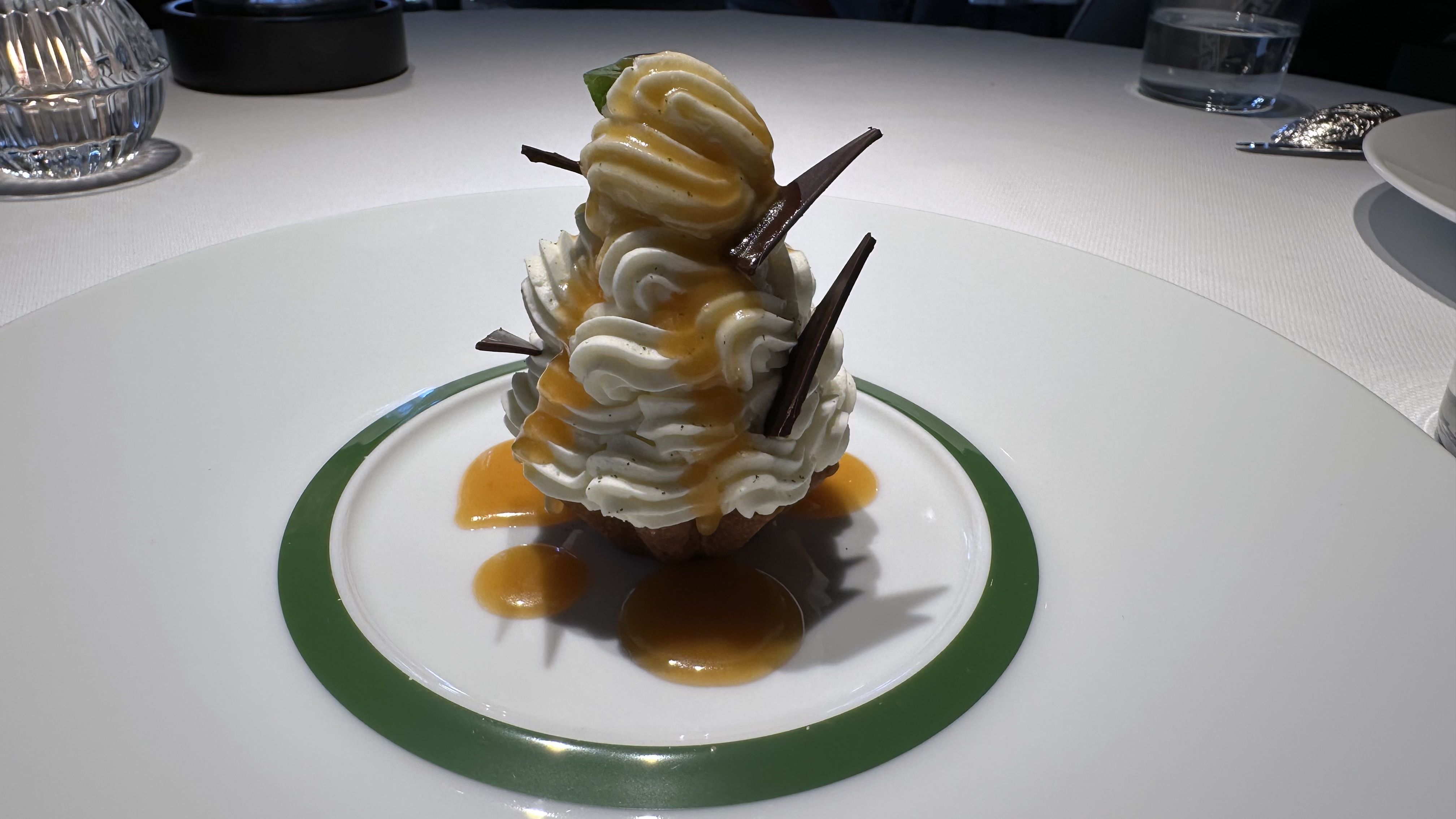 A small tart is topped with a tower of whipped cream and shards of chocolate.