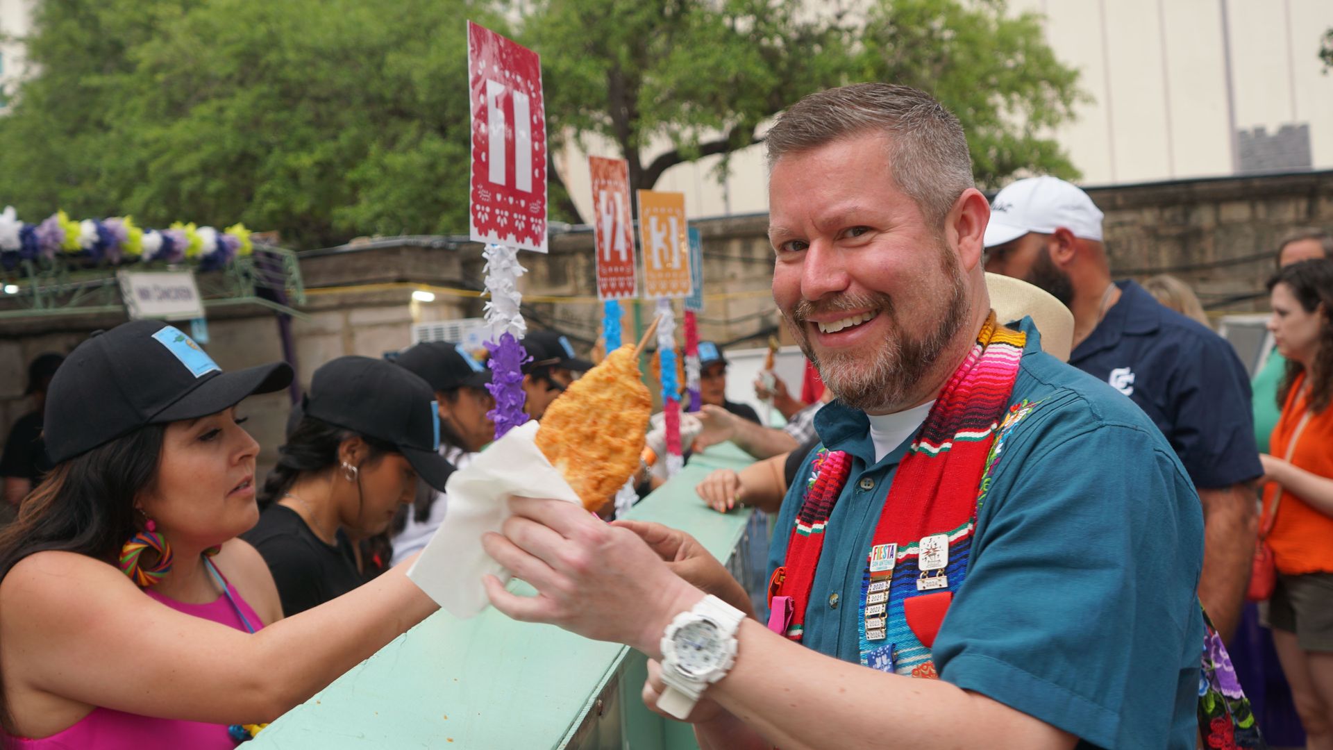 A man smiles while holding a skewered chicken patty.